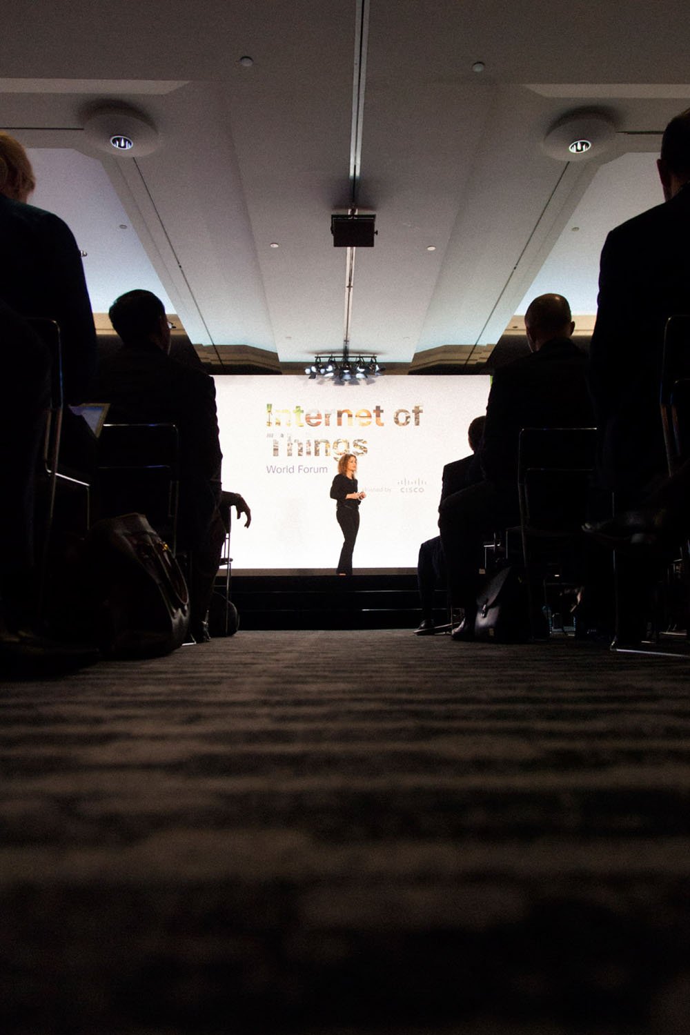 Conferencia en un auditorio con una presentadora en el escenario y una pantalla que dice 'Internet of Things'