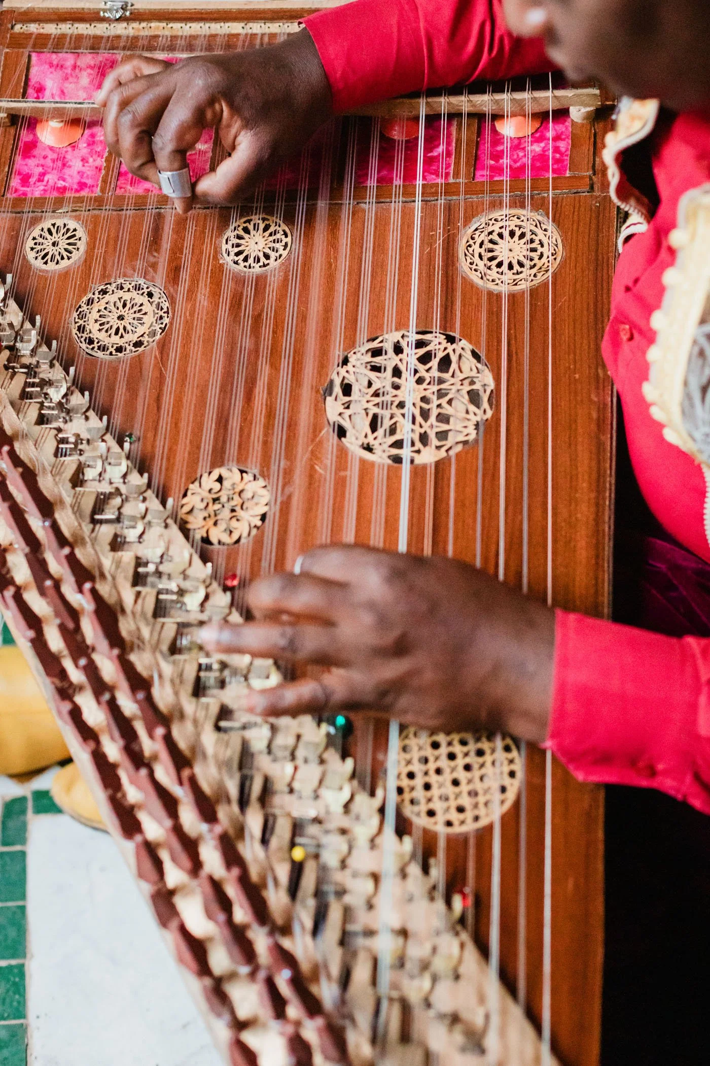 Persona tocando un instrumento musical de cuerda con múltiples cuerdas y patrones decorativos en la superficie de madera.