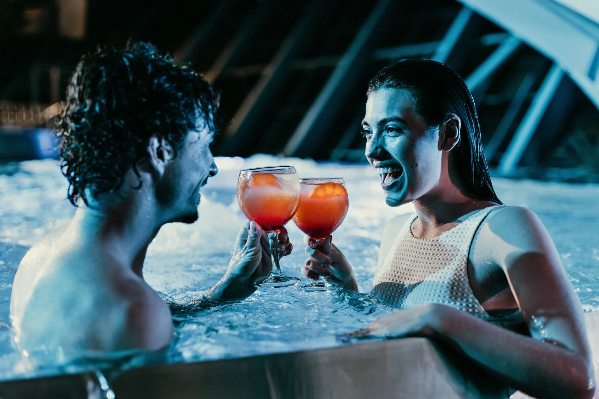 Dos personas felices en una tina, brindando con cócteles con hielo y fruta, en un ambiente alegre y relajado.