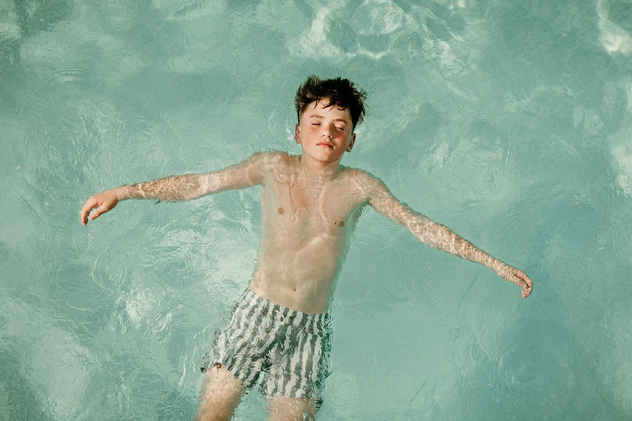 Joven en bañador disfrutando en una piscina con los ojos cerrados.