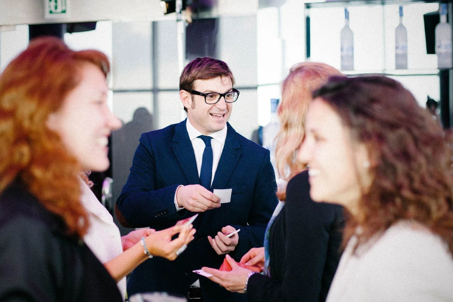 Un grupo de personas en una reunión, cuatro de ellas en primer plano y un hombre con gafas en el fondo sosteniendo tarjetas y sonriendo.