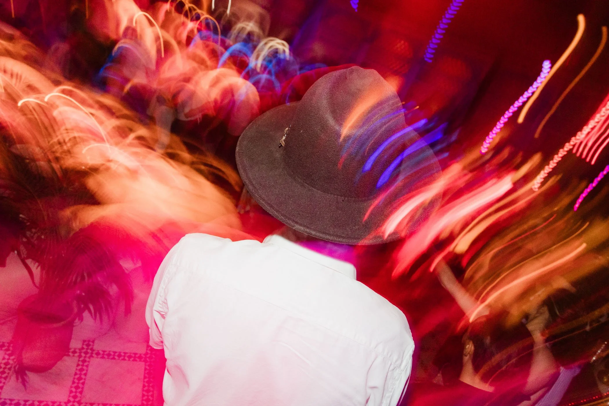 Persona con sombrero negro y camisa blanca en movimiento por la pista de baile con luces de colores