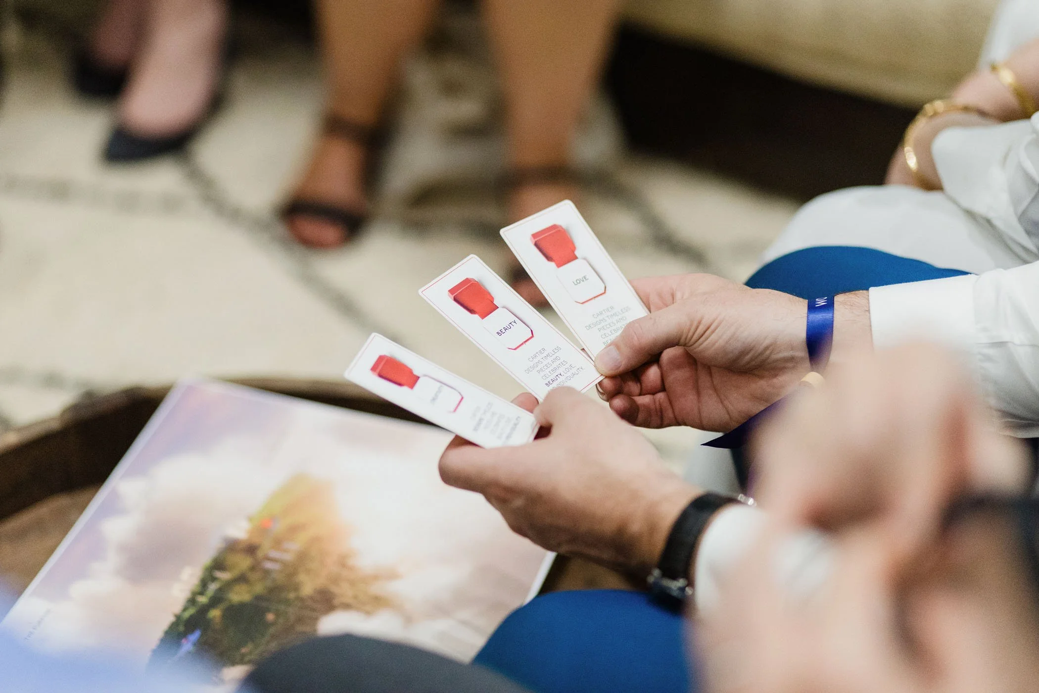 Persona sosteniendo folletos o tarjetas con palabras como "BEAUTY" y "LOVE" en un evento o reunión, con otras personas en el fondo.