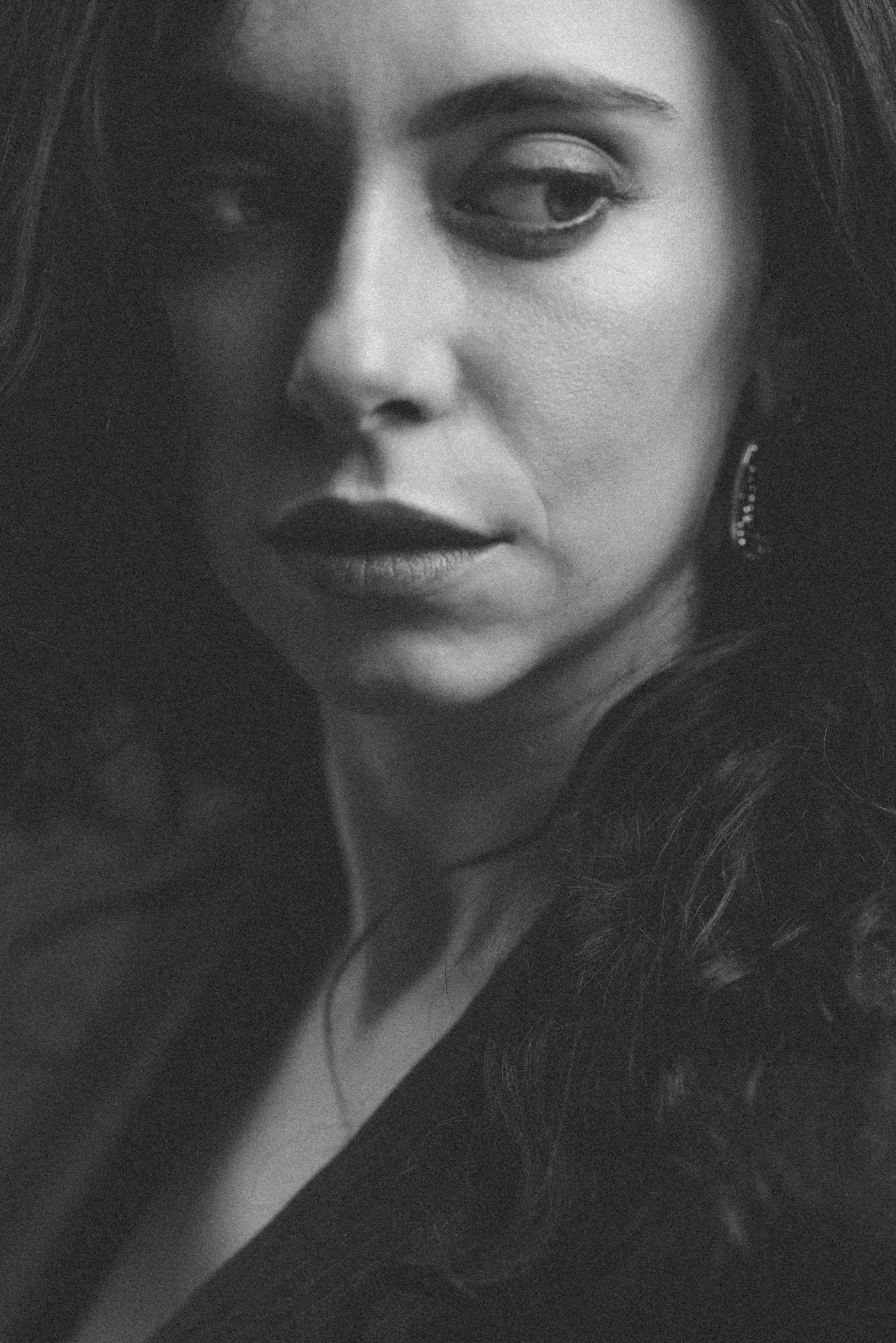 Retrato en blanco y negro de una mujer con cabello largo y suelto, con labios oscuros y mirada intensa, usando pendientes elegantes.