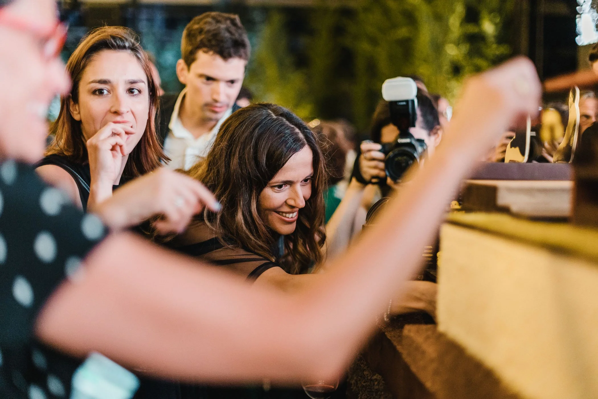 Grupo de personas en un evento nocturno, observando algo con interés, algunos toman fotografías, en un ambiente de celebración al aire libre.