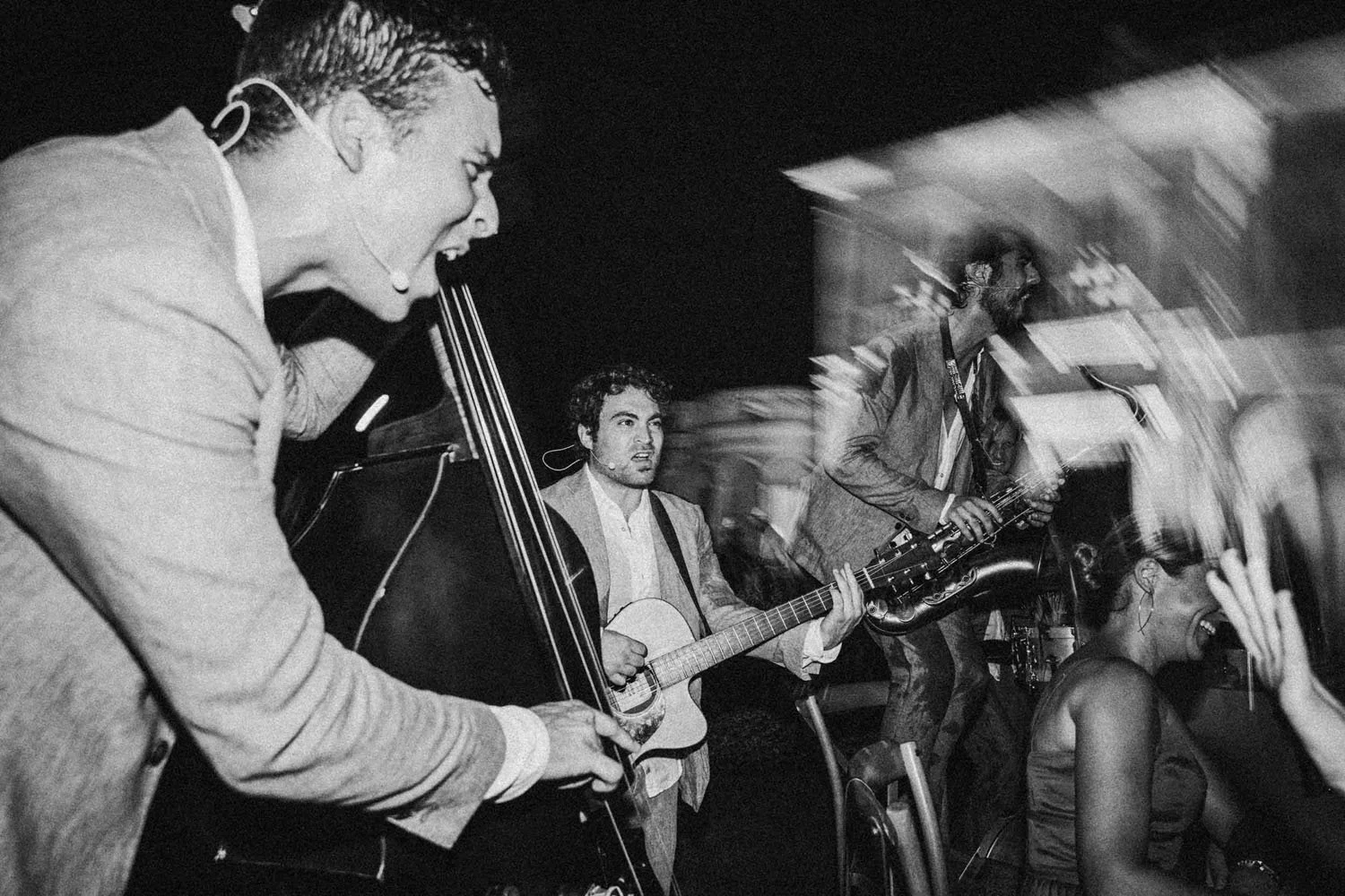 Grupo de músicos tocando instrumentos en un concierto, en blanco y negro, con movimiento y expresión de entusiasmo.