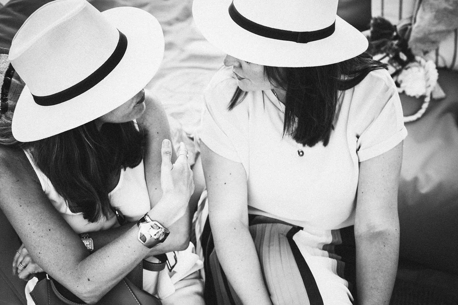 Dos mujeres con sombreros blancos y vestidos claros conversando en un entorno casual.