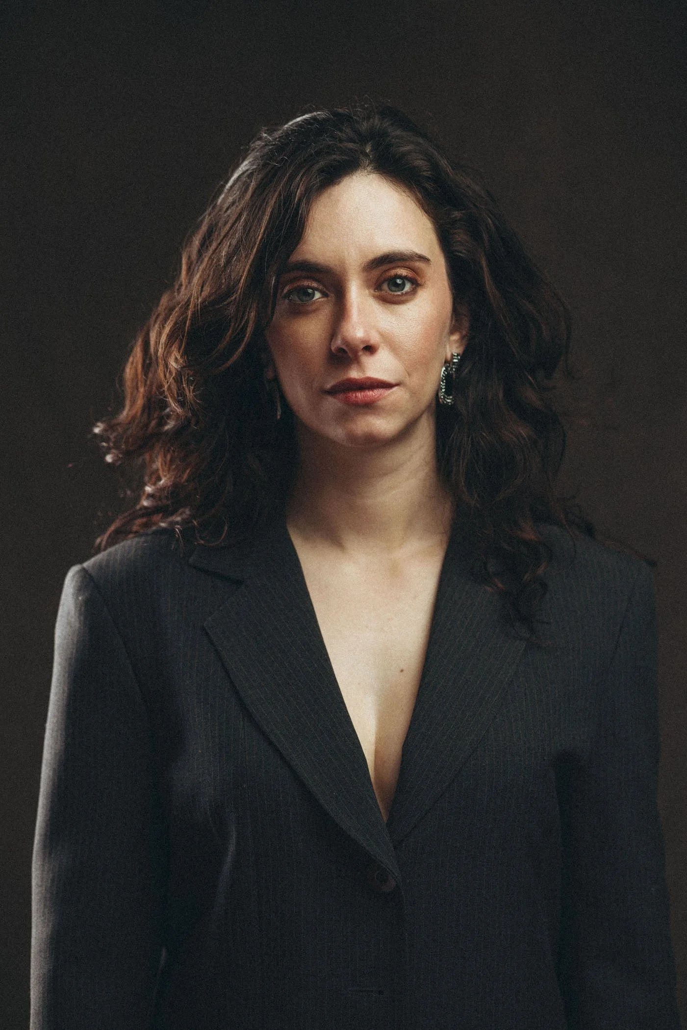 Retrato de una mujer con cabello rizado, vestida con un traje negro, mirando hacia la cámara con expresión seria