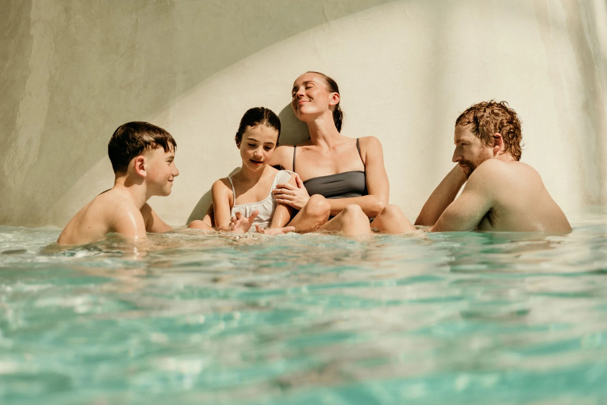 Familia feliz disfrutando en la piscina, calamando una mujer, un hombre y dos niños pequeños.