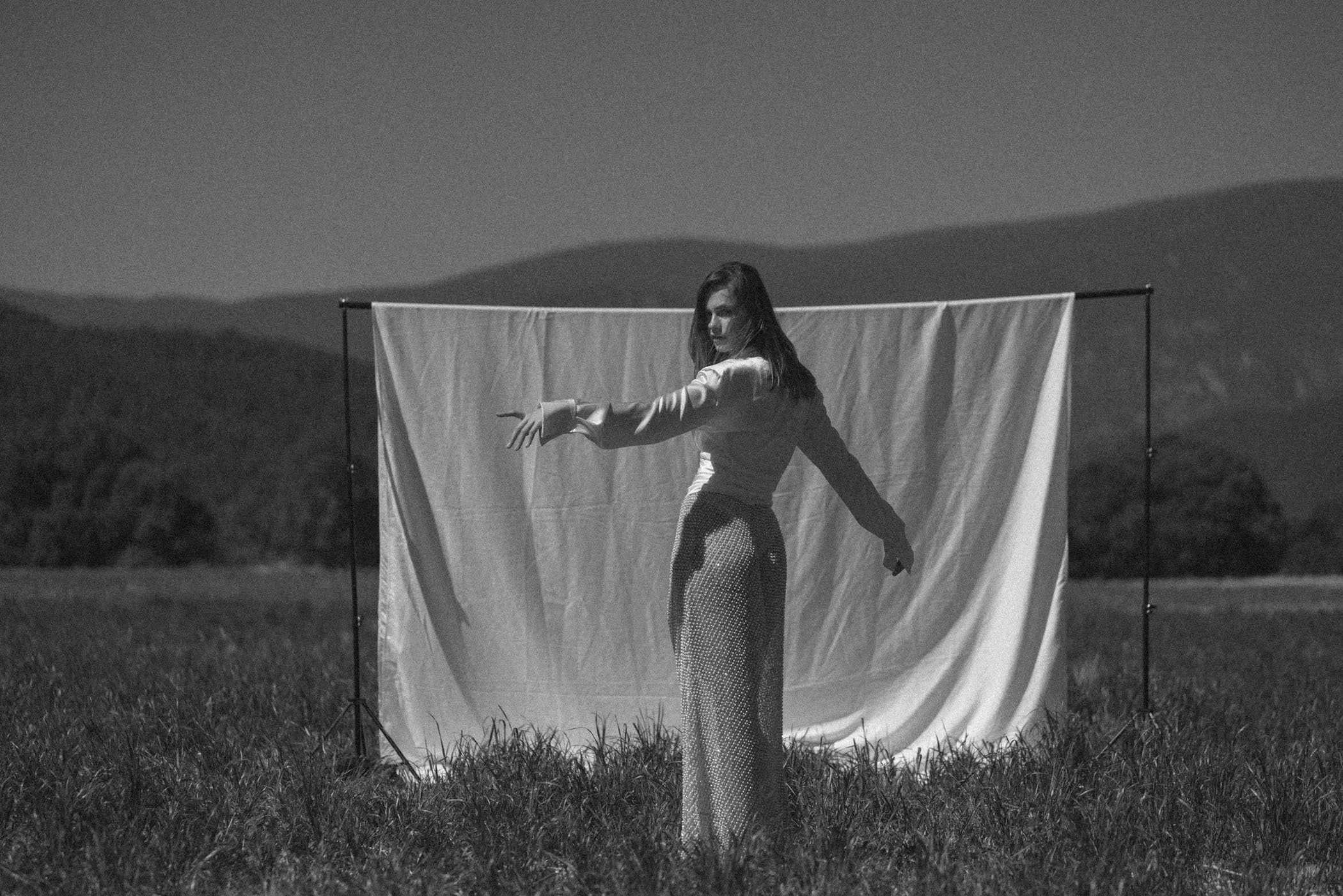 Mujer en un campo sostenido en un fondo de cortina, en un contexto de fotografía en blanco y negro.