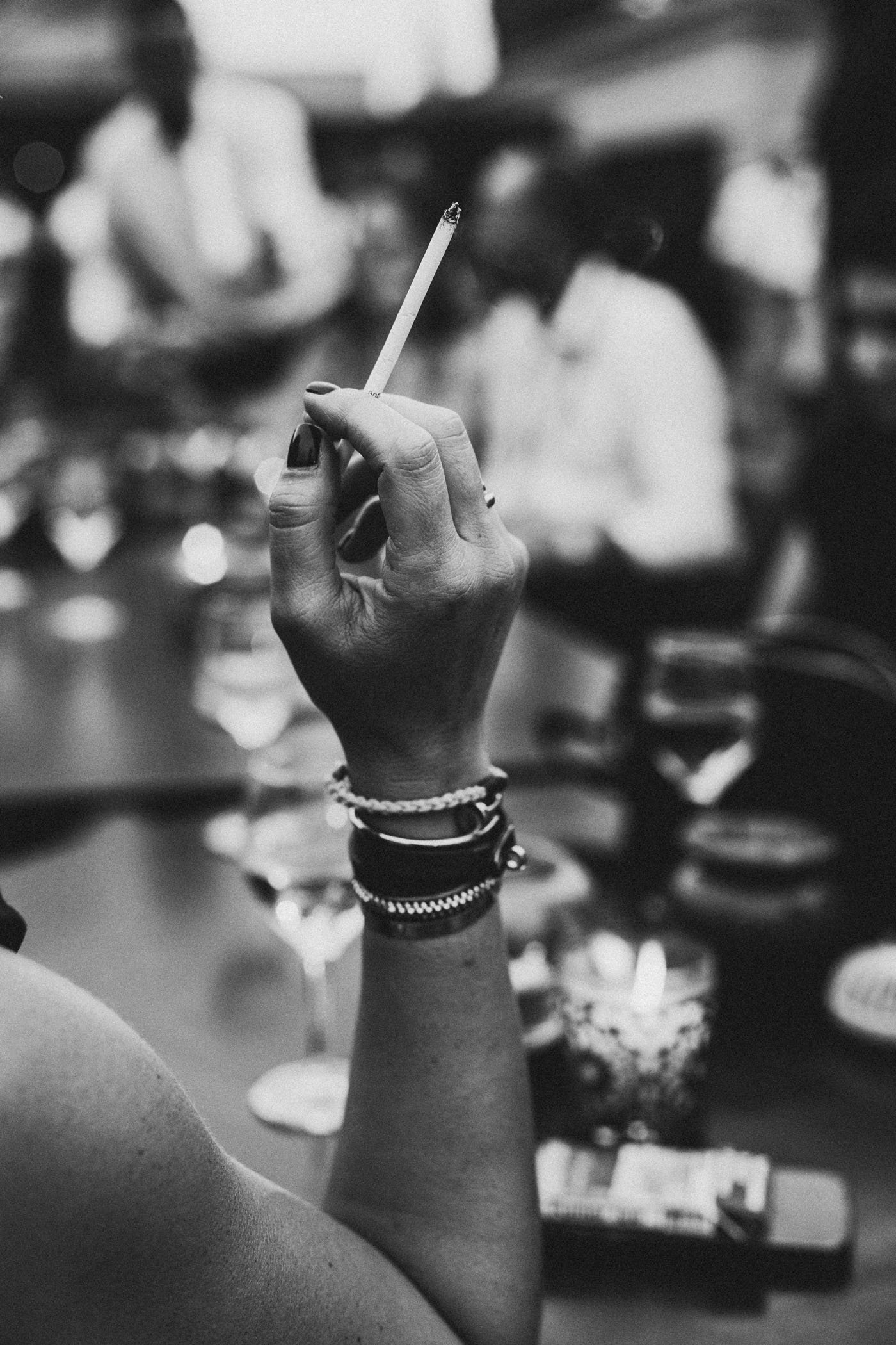 Mano sosteniendo un cigarrillo en un ambiente social, con personas en el fondo
