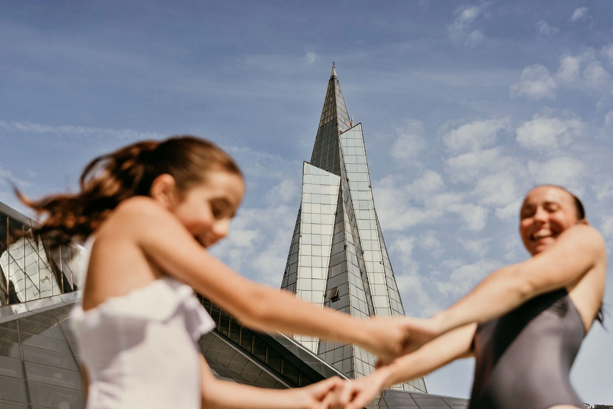 Dos mujeres jugando con una cuerda con un edificio moderno de fondo bajo un cielo con nubes.