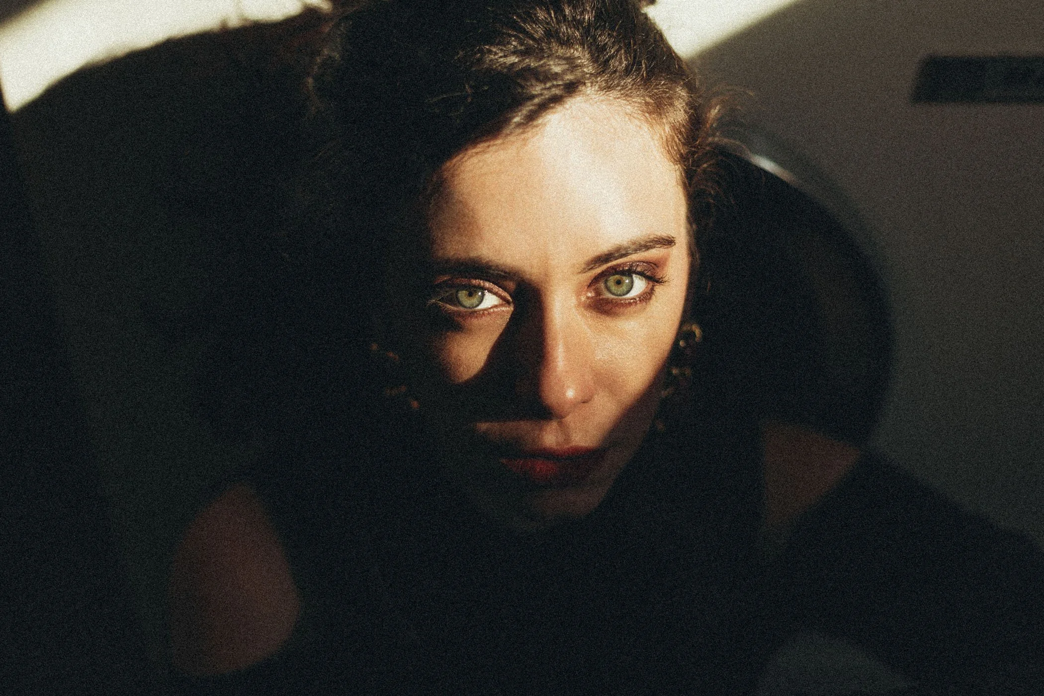 Retrato en primer plano de una mujer con cabello oscuro y ojos verdes, con luz que ilumina su rostro desde arriba.