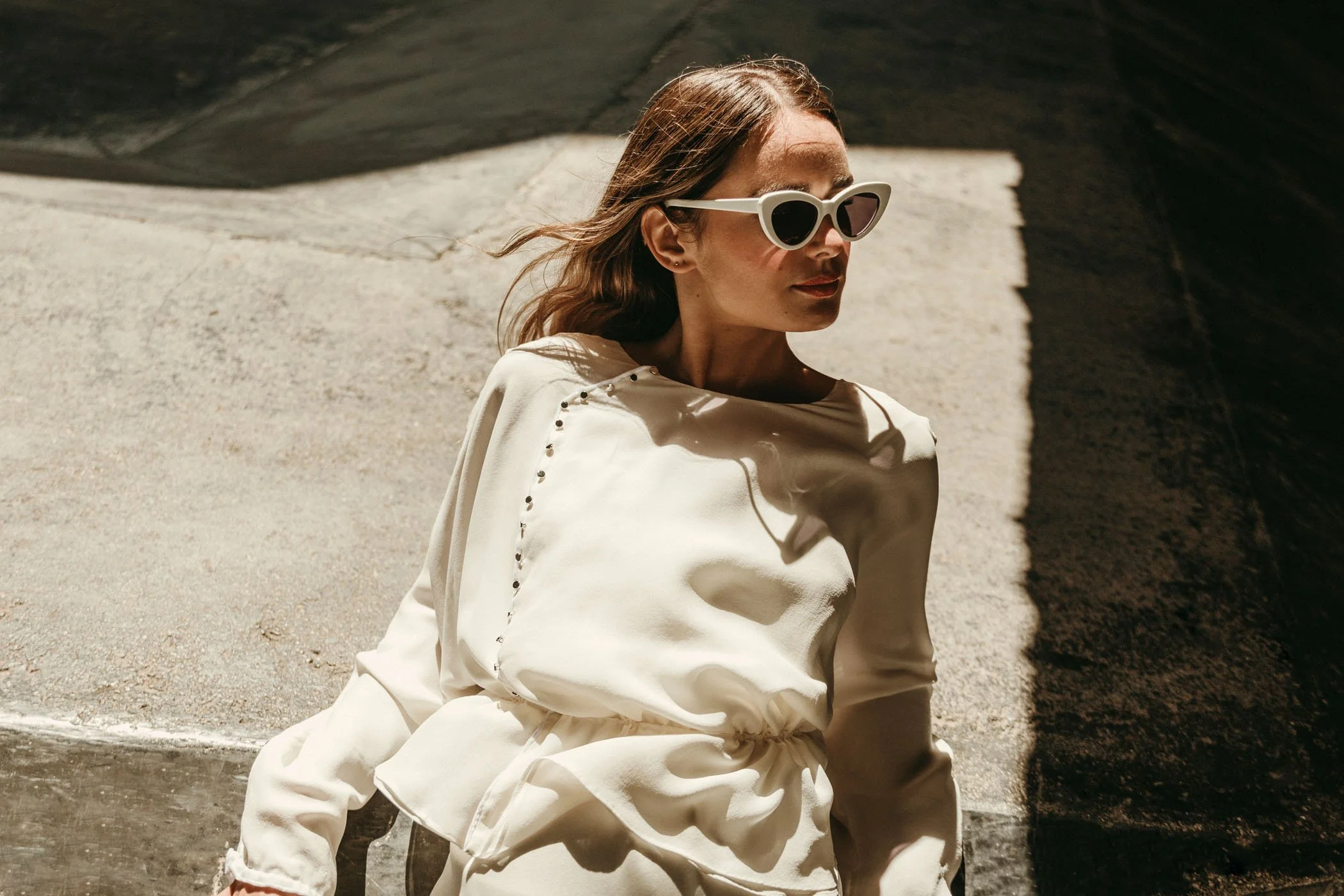 Mujer con gafas de sol blancas y blusa blanca en un ambiente soleado y con sombra.