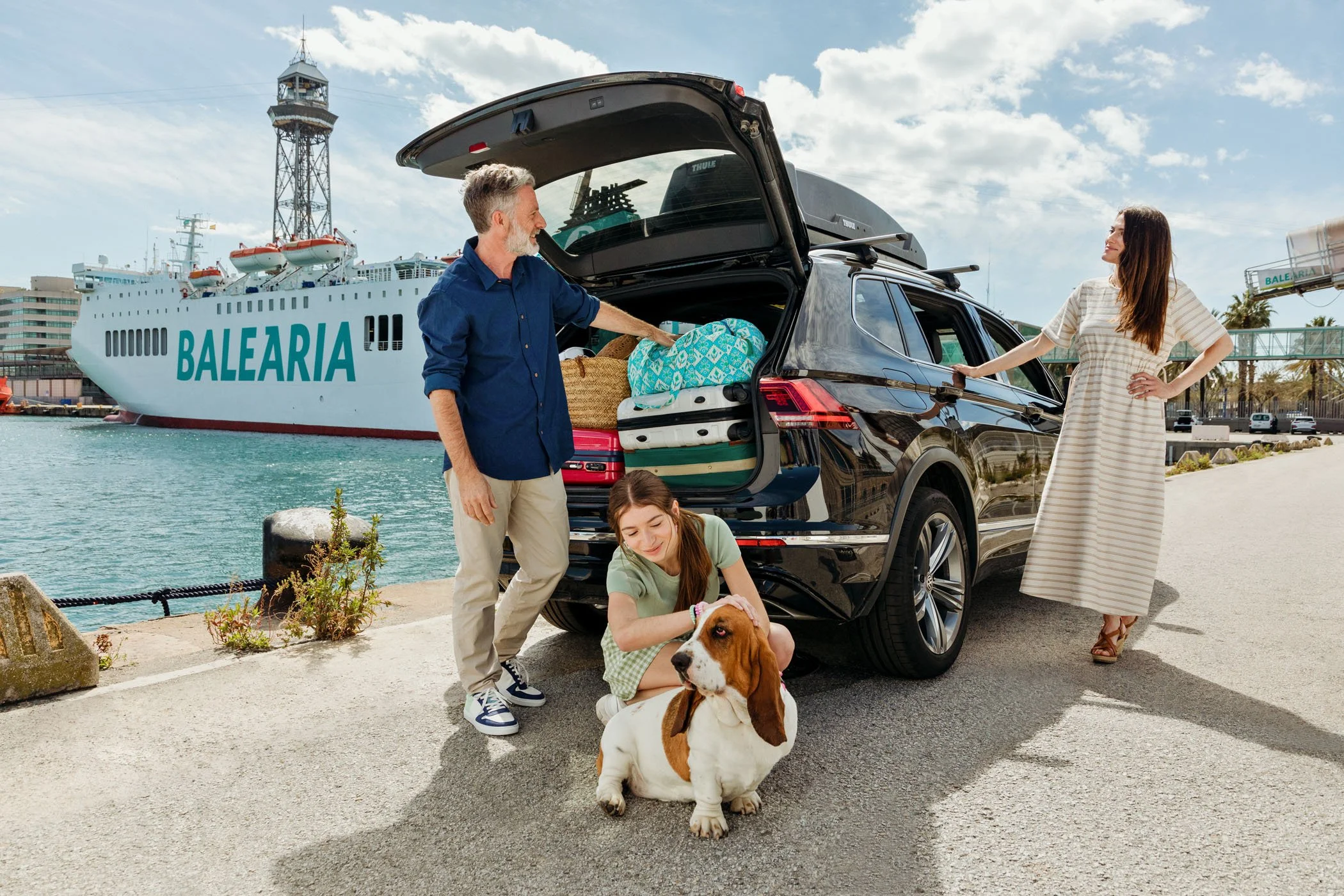 familia preparándose para un viaje cerca del mar con un ferry llamado 'Balearia' en el fondo, junto a un coche negro con maletas y un perro beagle.