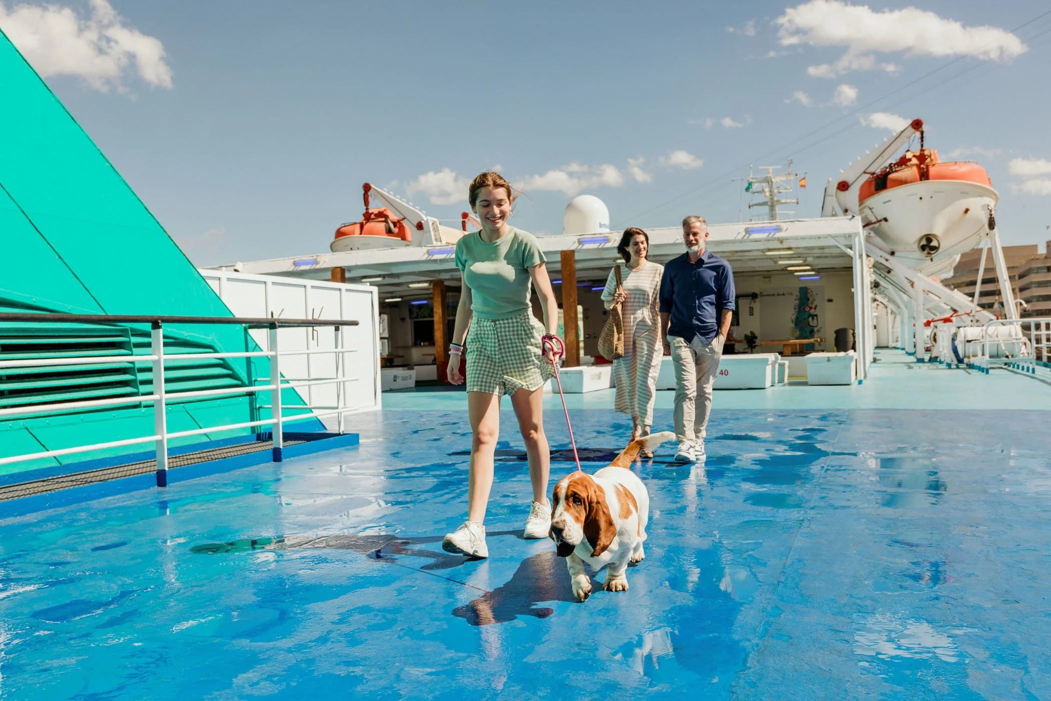 Personas caminando en la cubierta de un barco con un perro de raza basset hound en un día soleado