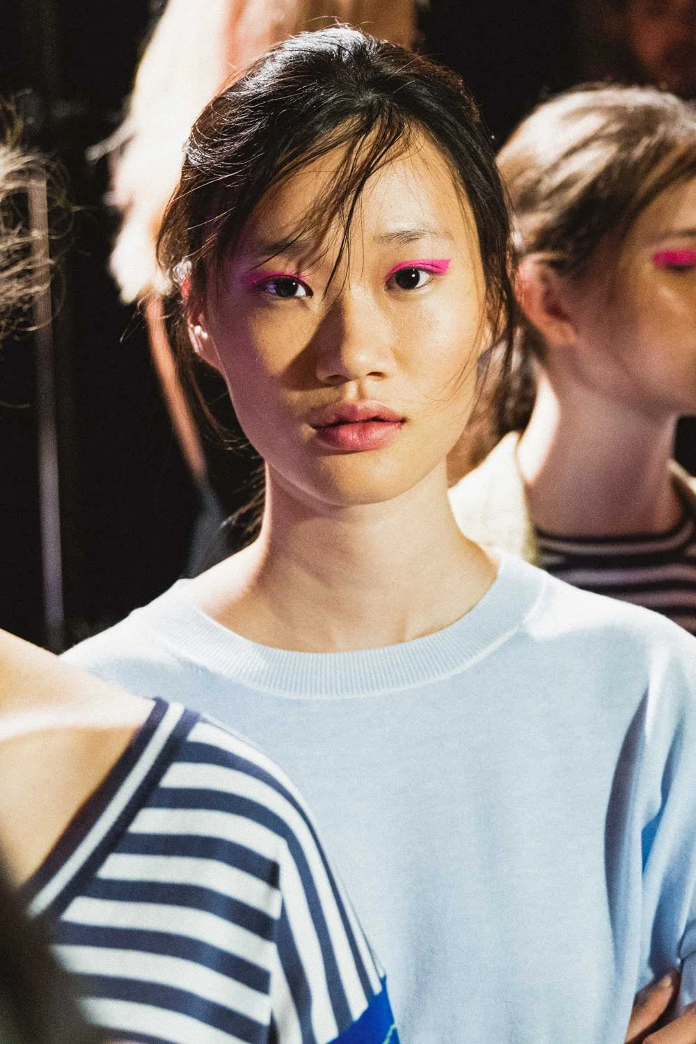 Mujer joven con maquillaje de delineador rosa y labios nude en un entorno de moda.