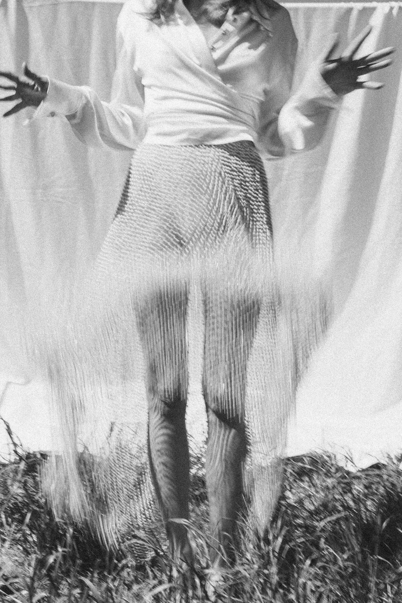 Mujer de vestido largo y blusa, posando en un entorno natural, en blanco y negro.