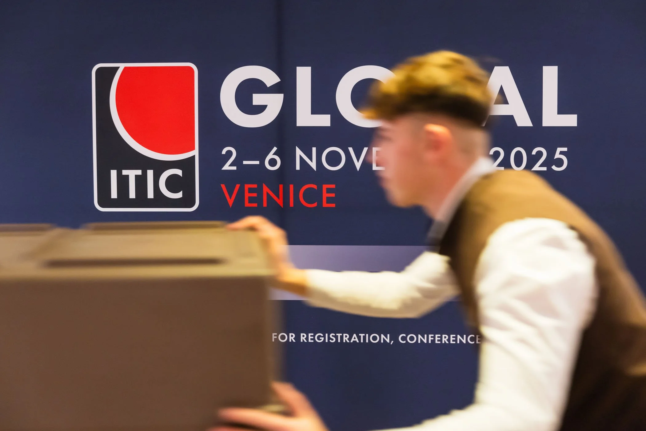 Foto de un hombre que empuja una mesa o mostrador en un evento titulado 'Glocal' en Venecia, del 2 al 6 de noviembre de 2025, organizado por ITIC.