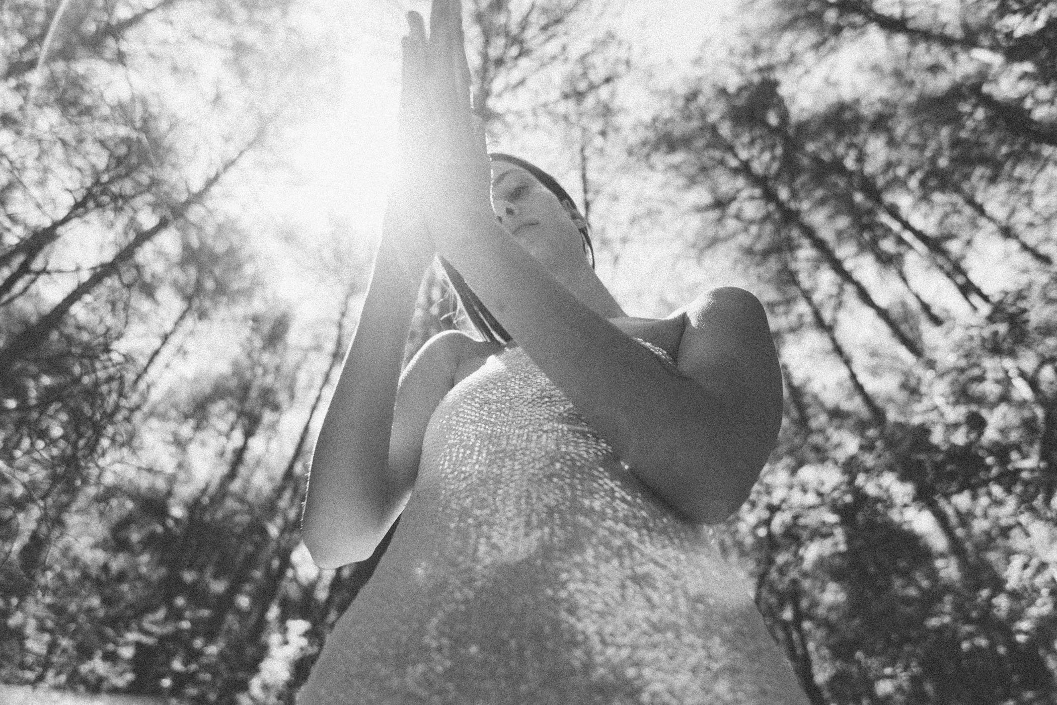 Mujer con vestido de noche y sombrero, en un bosque con árboles y luz solar brillante.