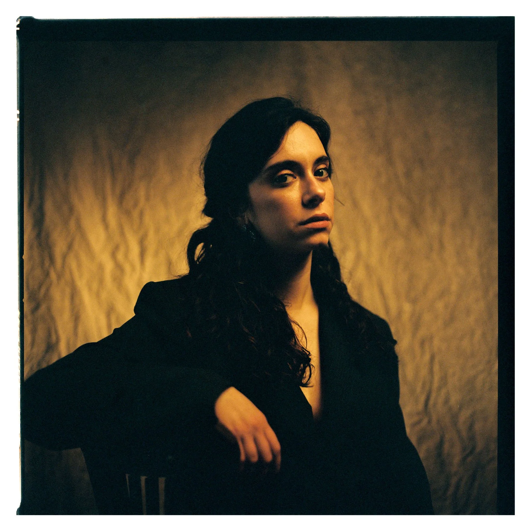 Retrato de una mujer con cabello oscuro y rizado, vestida con ropa negra, con fondo de color marrón y textura suave.