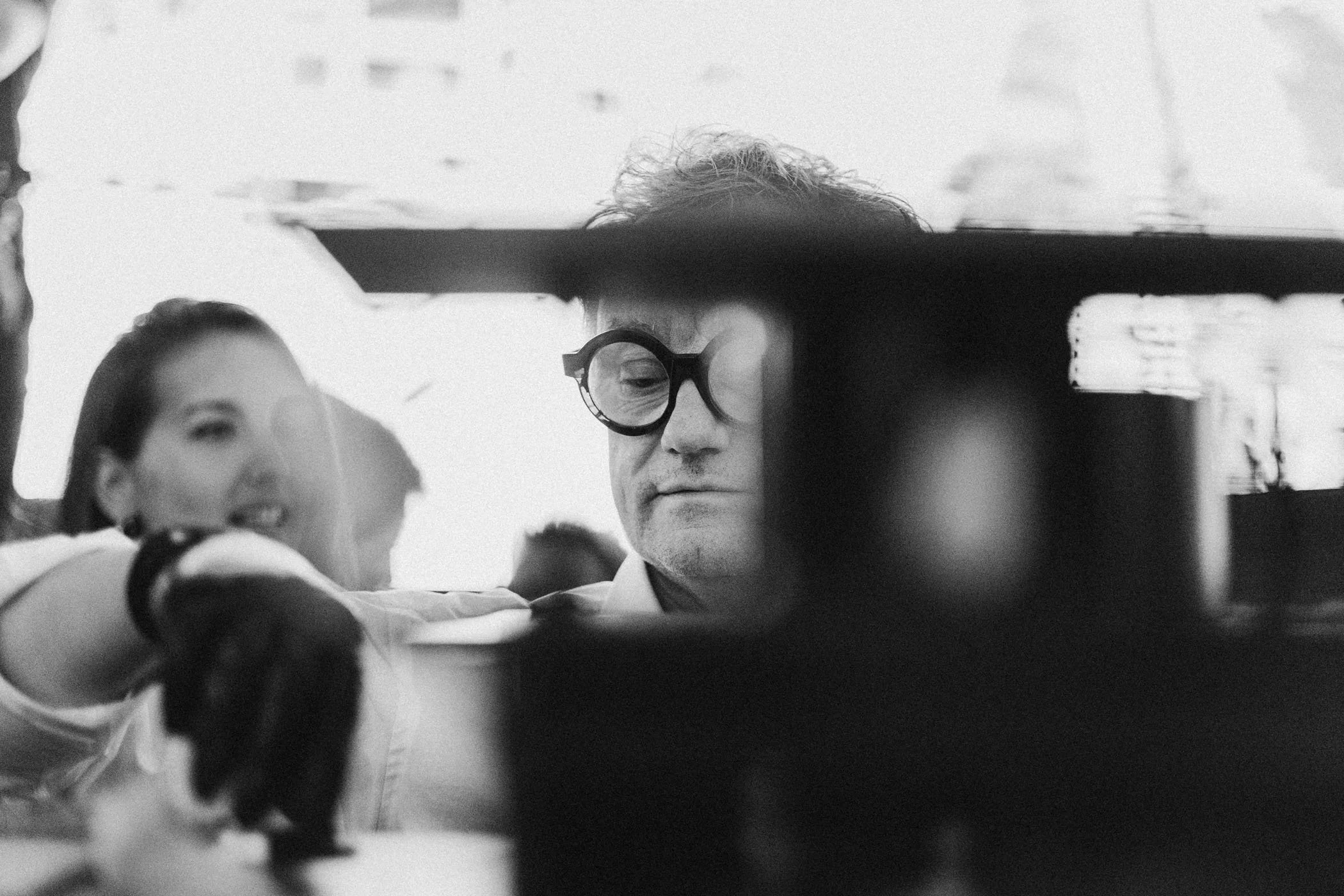 Hombre con gafas grandes y mujer con cabello largo en un entorno urbano, en blanco y negro.