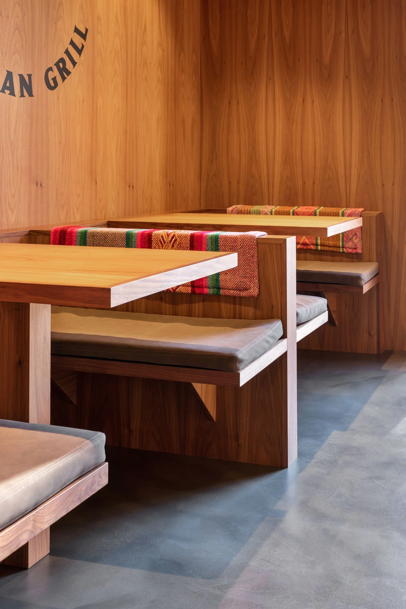 Una esquina en un restaurante con paredes de madera y mesas de madera con bancos acolchonados y manteles tejidas de colores.