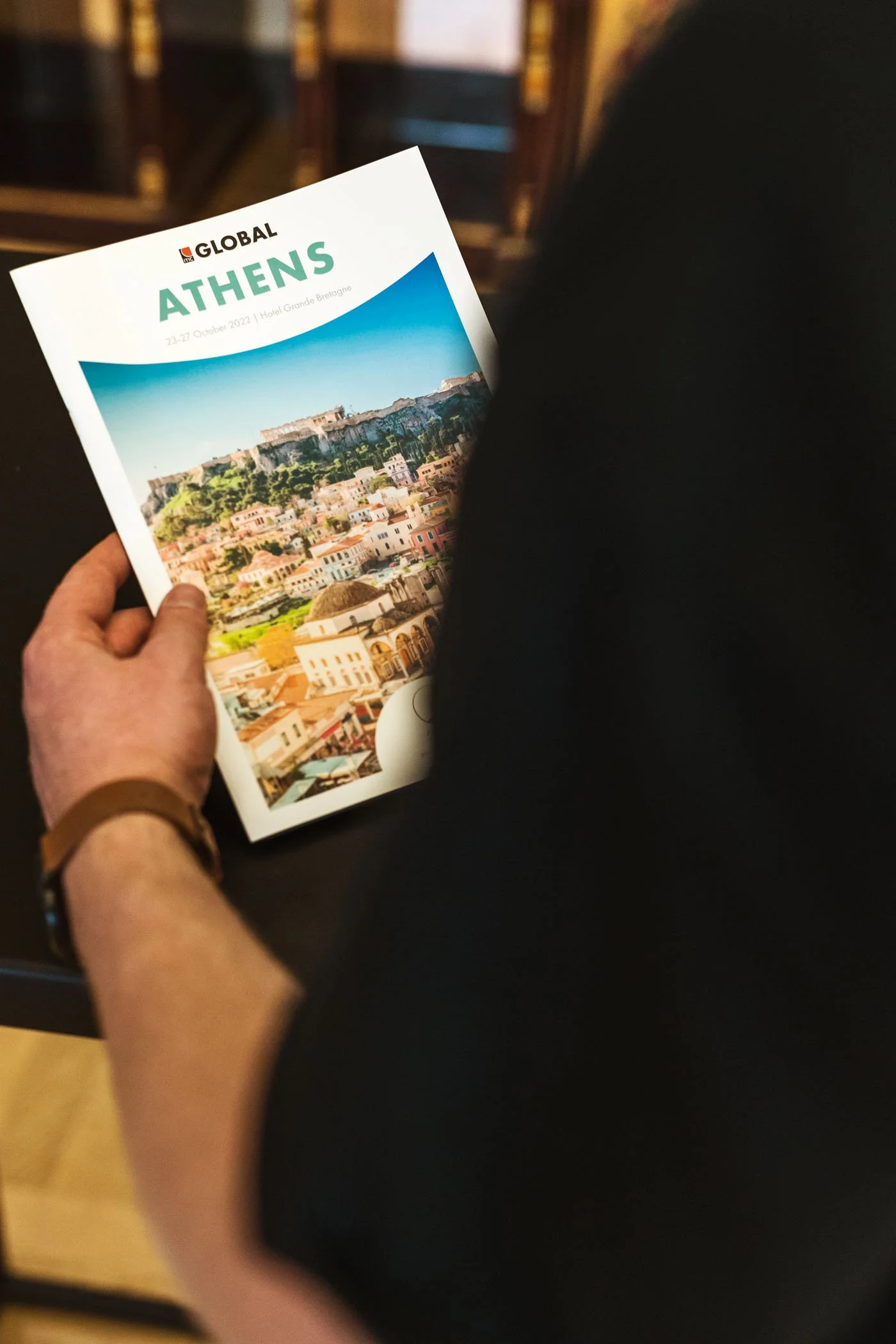 Persona sosteniendo un folleto con la inscripción 'Global Athens' y una imagen de la ciudad de Atenas en Grecia.