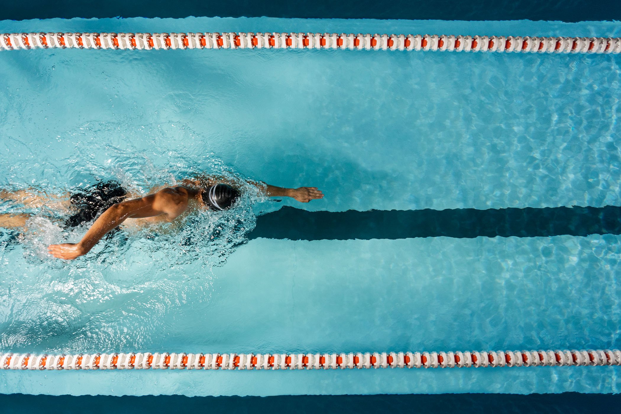 Persona nadando en una piscina con gorro negro, vista aérea.