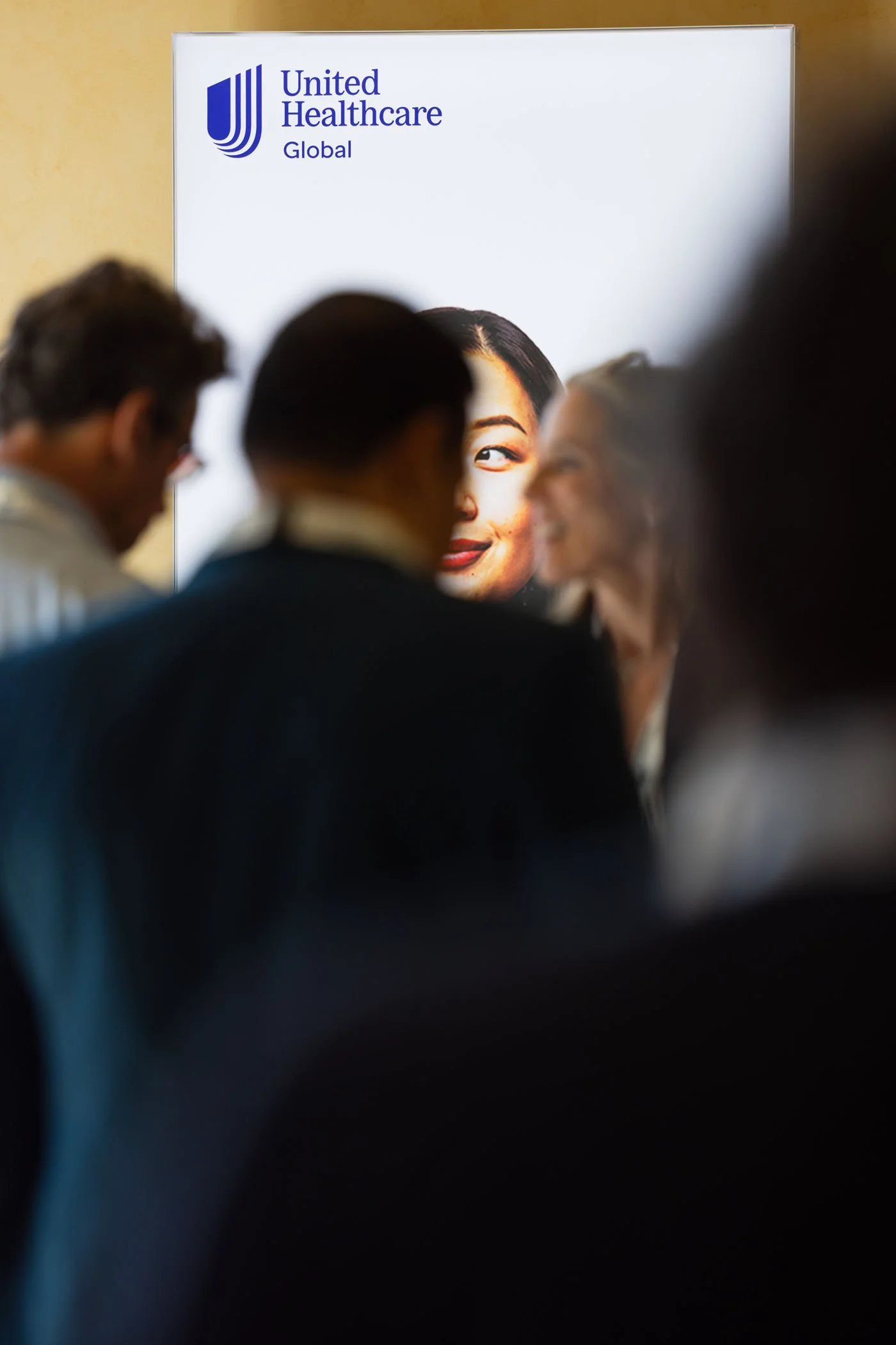 Personas en un evento de United Healthcare Global, con un cartel en el fondo que muestra un rostro femenino y el logotipo de la compañía.