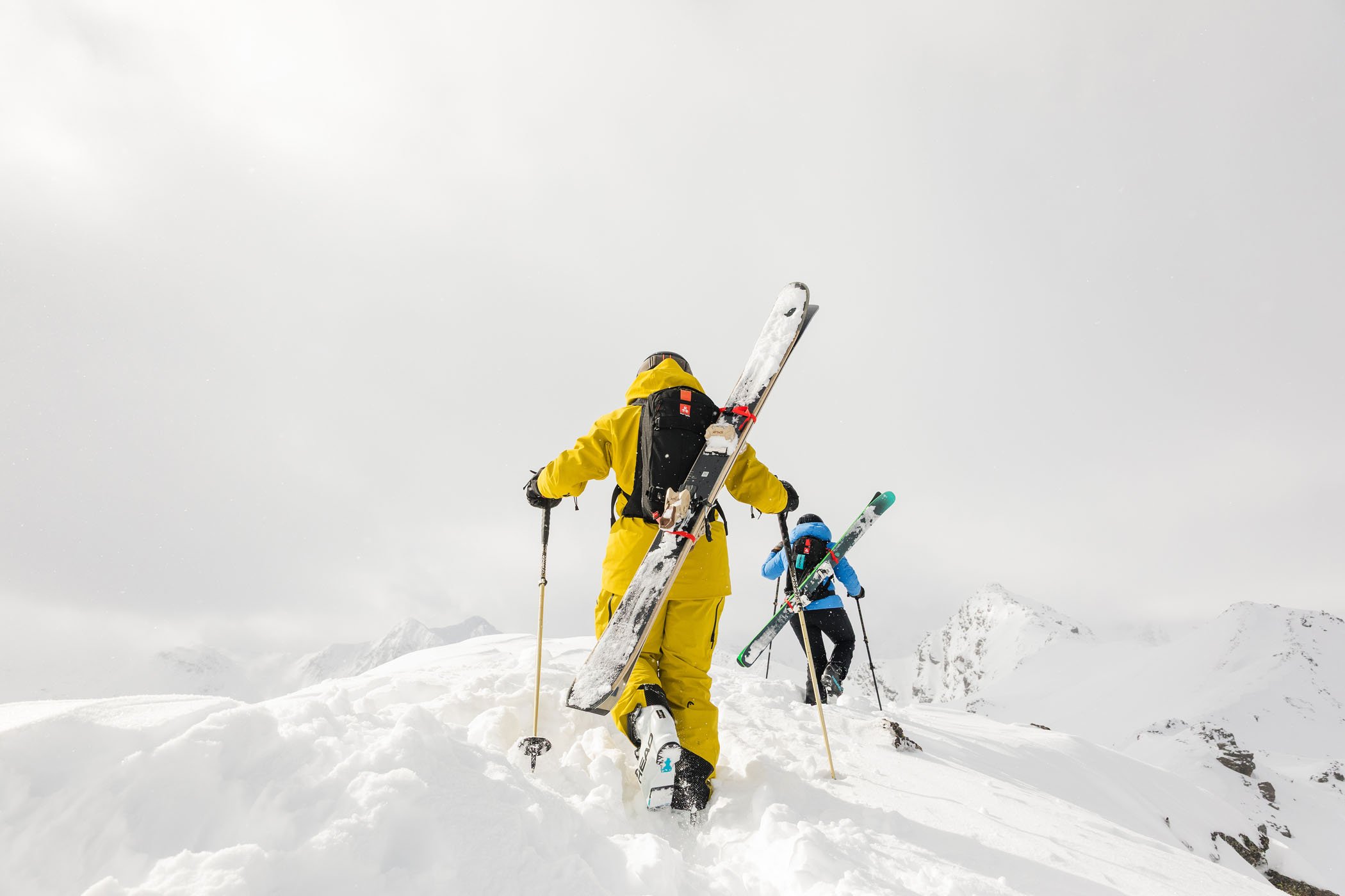 Dos esquiadores caminando en la nieve en una montaña cubierta de nieve con cielo nublado.