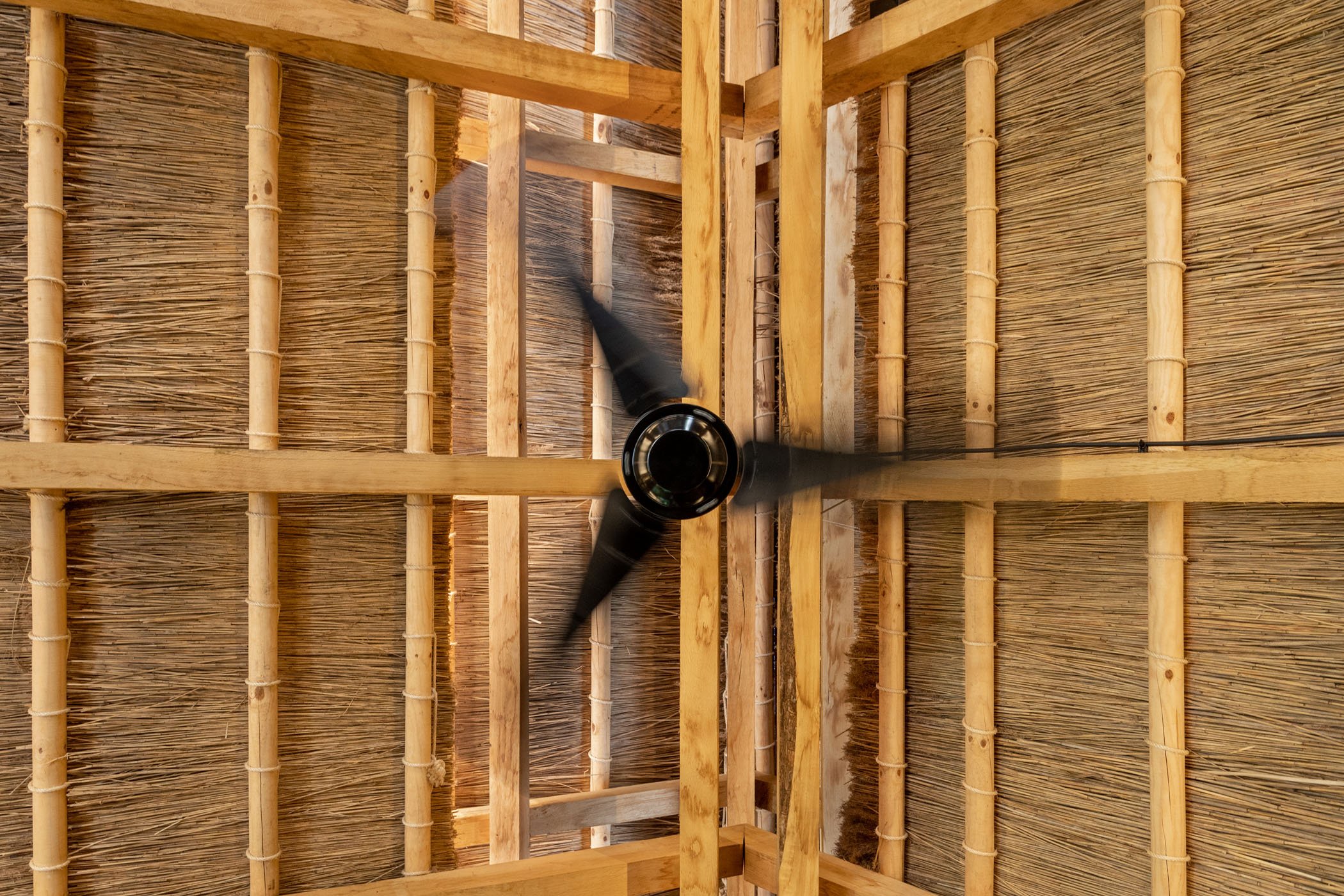 Ventilador de techo en construcción con estructura de madera y paredes de paja.