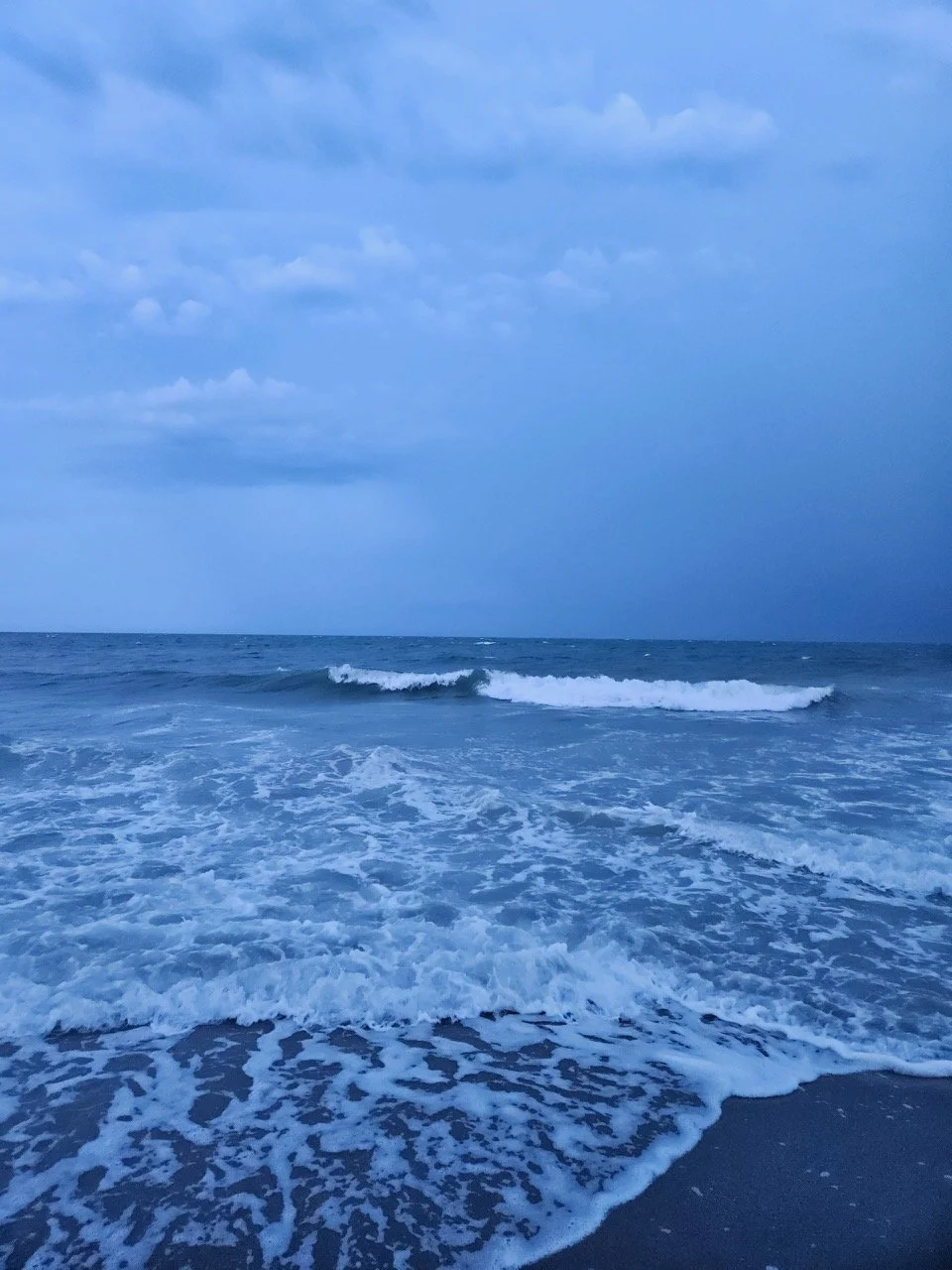 Ocean waves crashing on the shore during a cloudy evening.