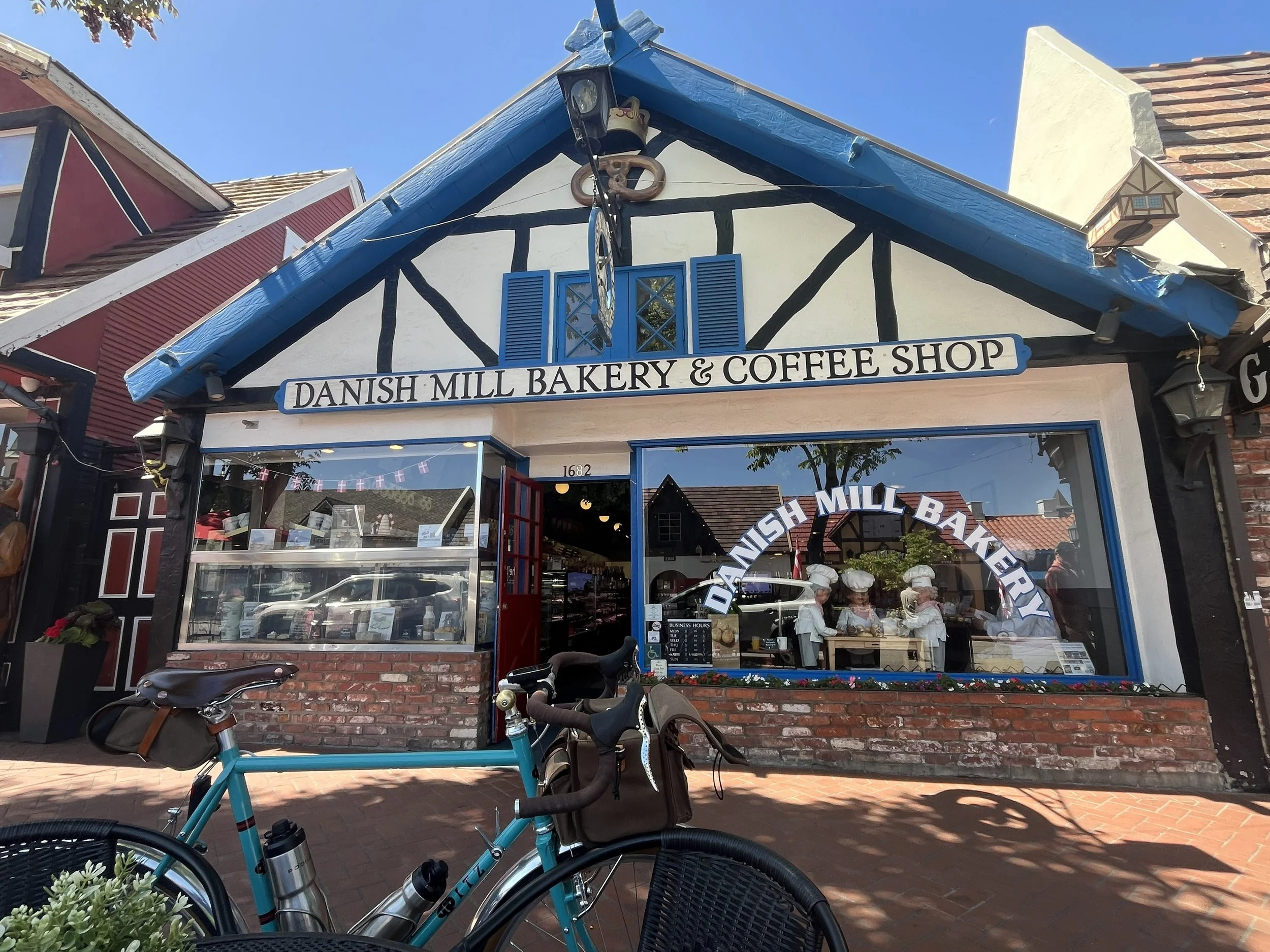 Exterior of Danish Mill Bakery & Coffee Shop with bicycles parked in front and a sign above the entrance.