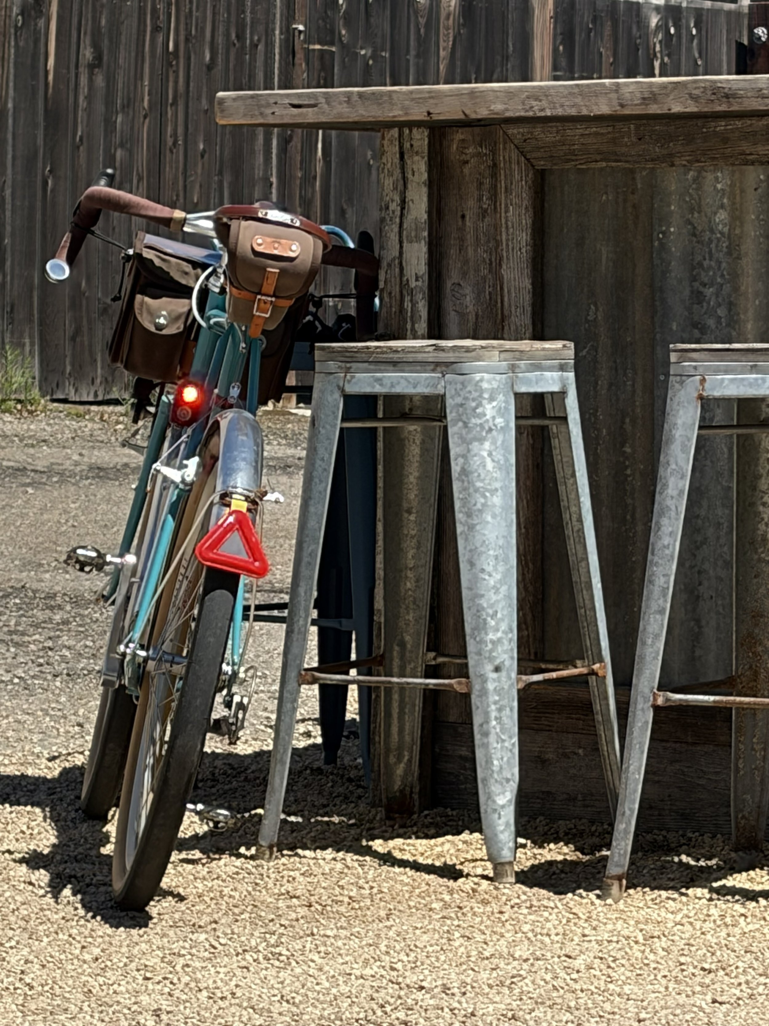 A vintage bicycle resting against a wooden fence on a gravel surface.