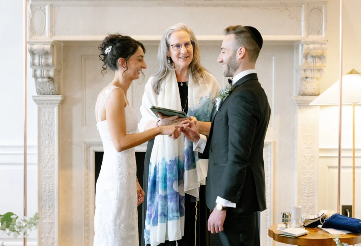 A wedding ceremony with a bride and groom exchanging vows, an officiant officiating, in a decorated room.