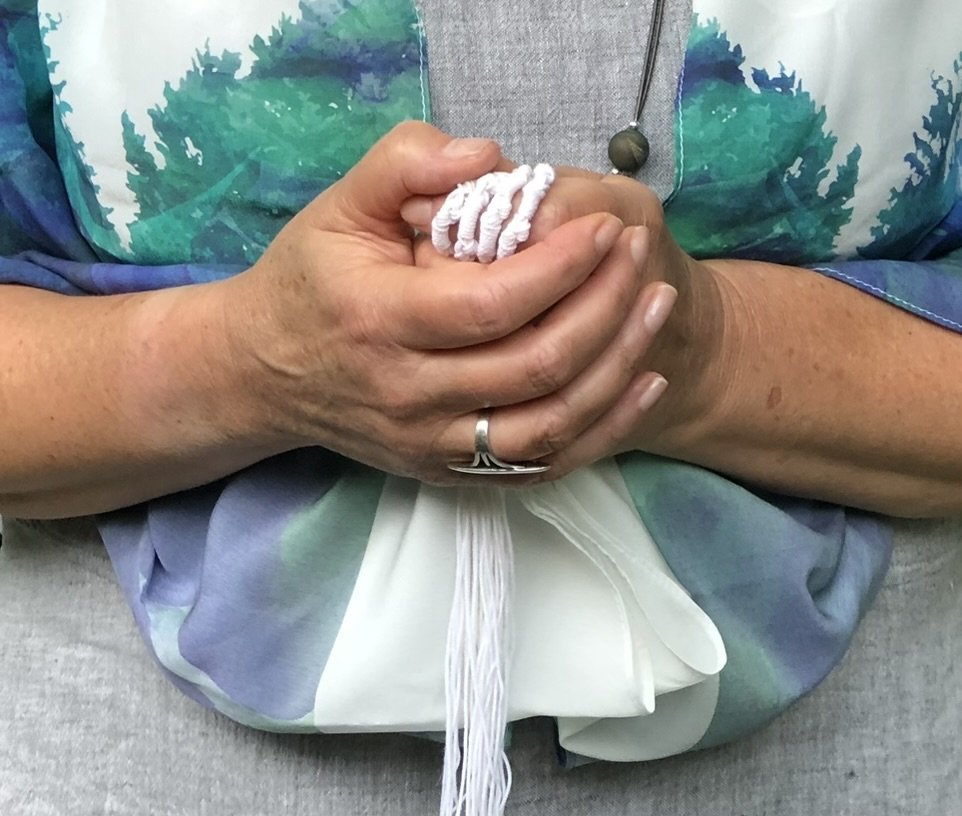 Person holding a bundle of white yarn in their hands, wearing a multi-colored jacket and sitting on a light-colored surface.