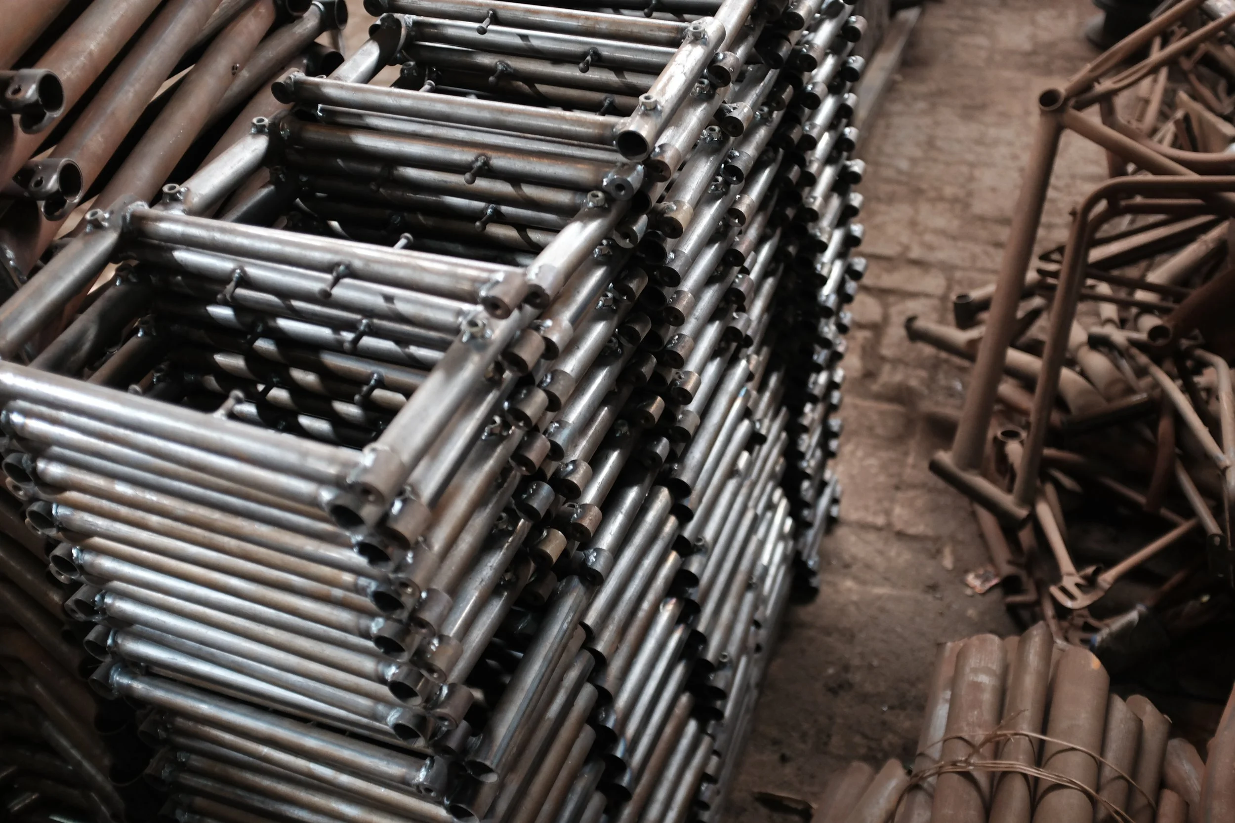 Stacks of metal pipes and metal scraper tools on a dirt floor.