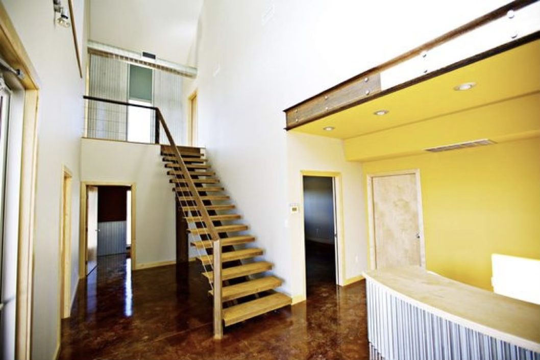 Interior of a modern house with a central staircase, yellow accent wall, and wooden finishes.