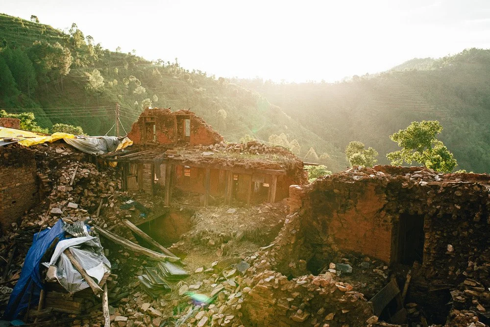 Ruined brick buildings in a mountainous area with sunlight shining through, debris scattered around.