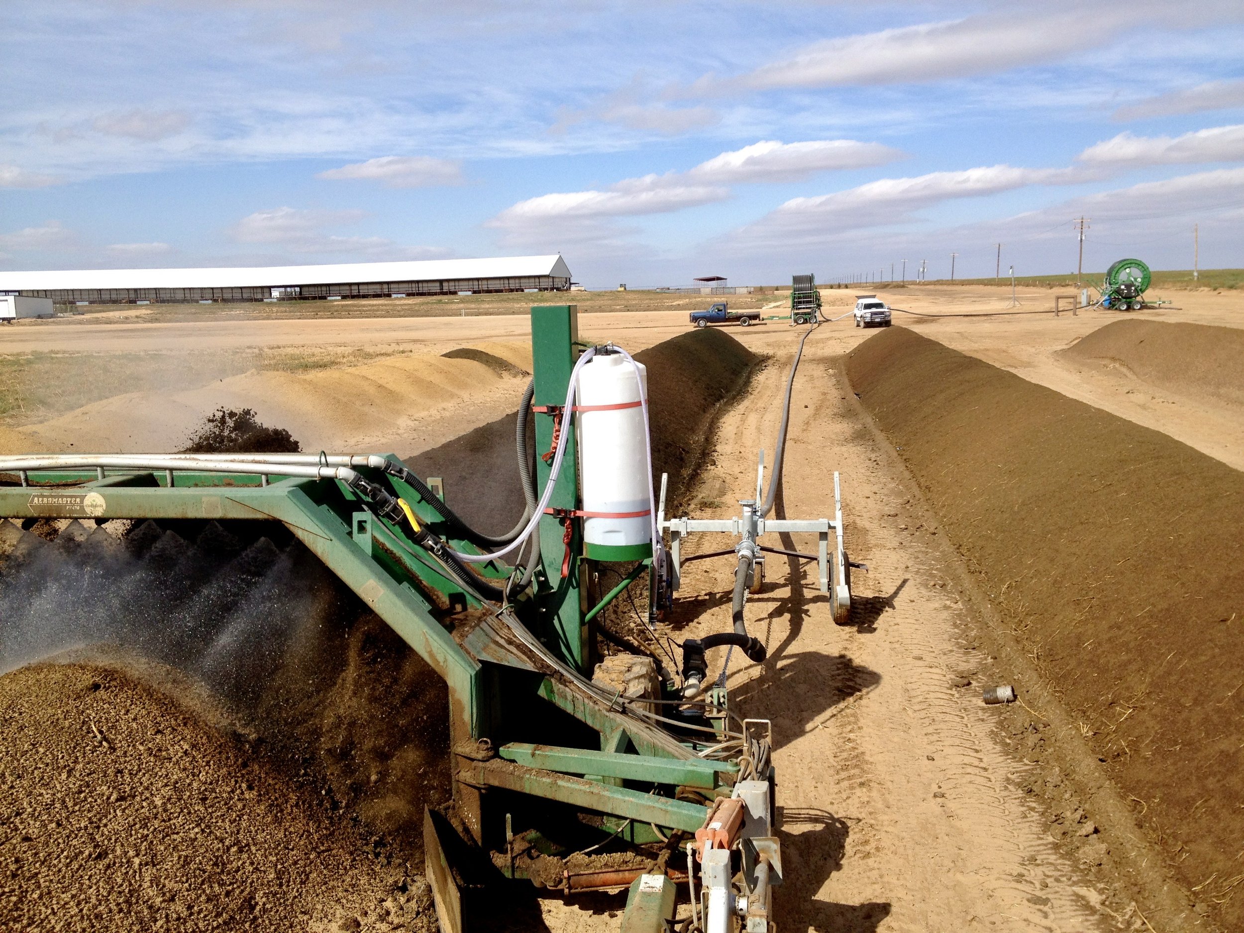 Agricultural machinery working on a field with mounds of soil, under a partly cloudy sky.