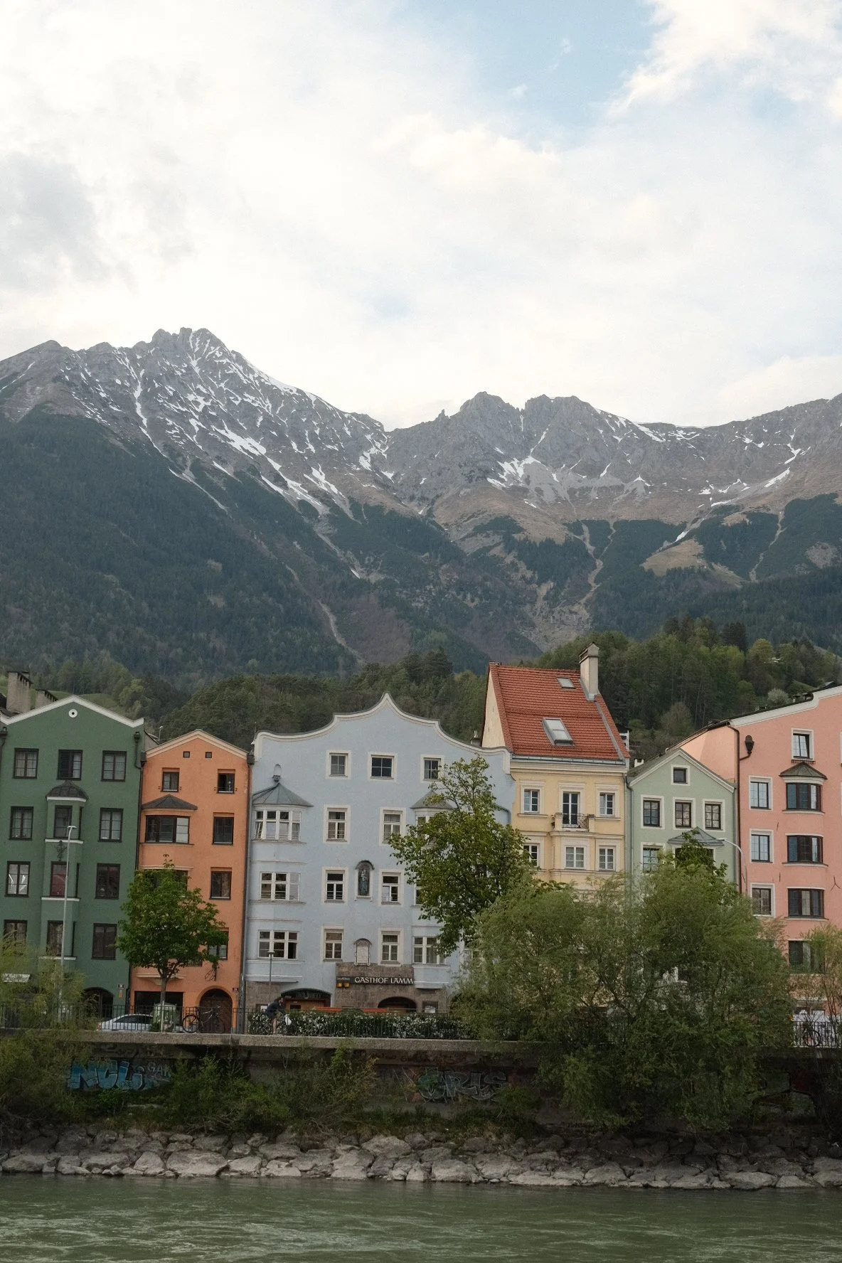 Colorful European-style buildings along a riverside with mountains in the background.