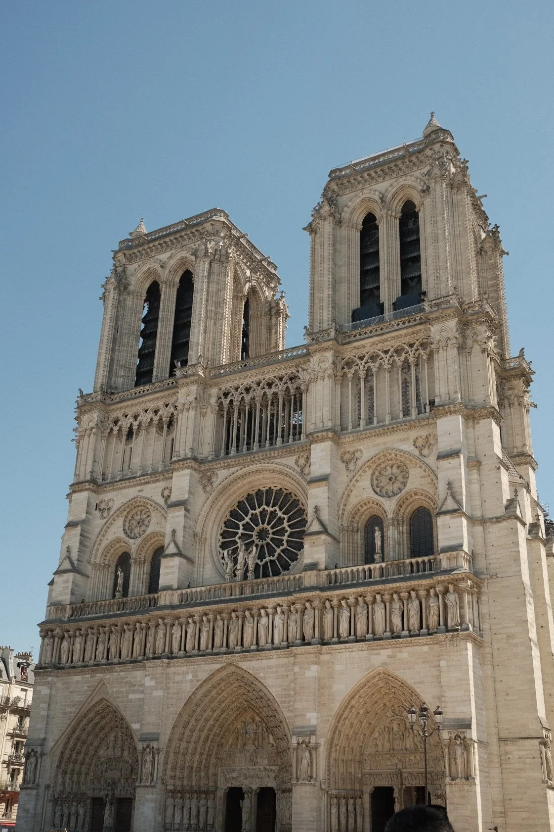 The front view of the Notre-Dame Cathedral in Paris with detailed Gothic architecture, twin towers, and rose window under a clear blue sky.