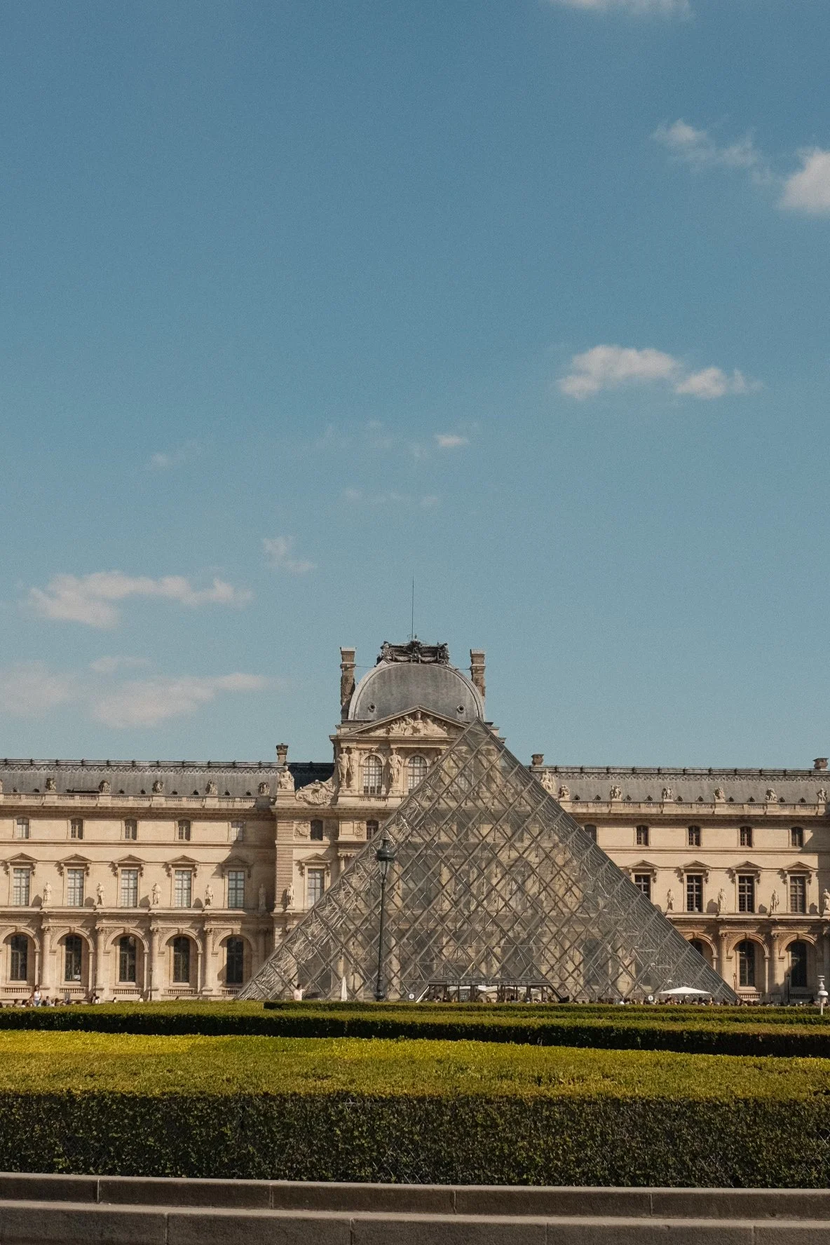 The Louvre Museum with its glass pyramid entrance in Paris, France, under a clear blue sky.