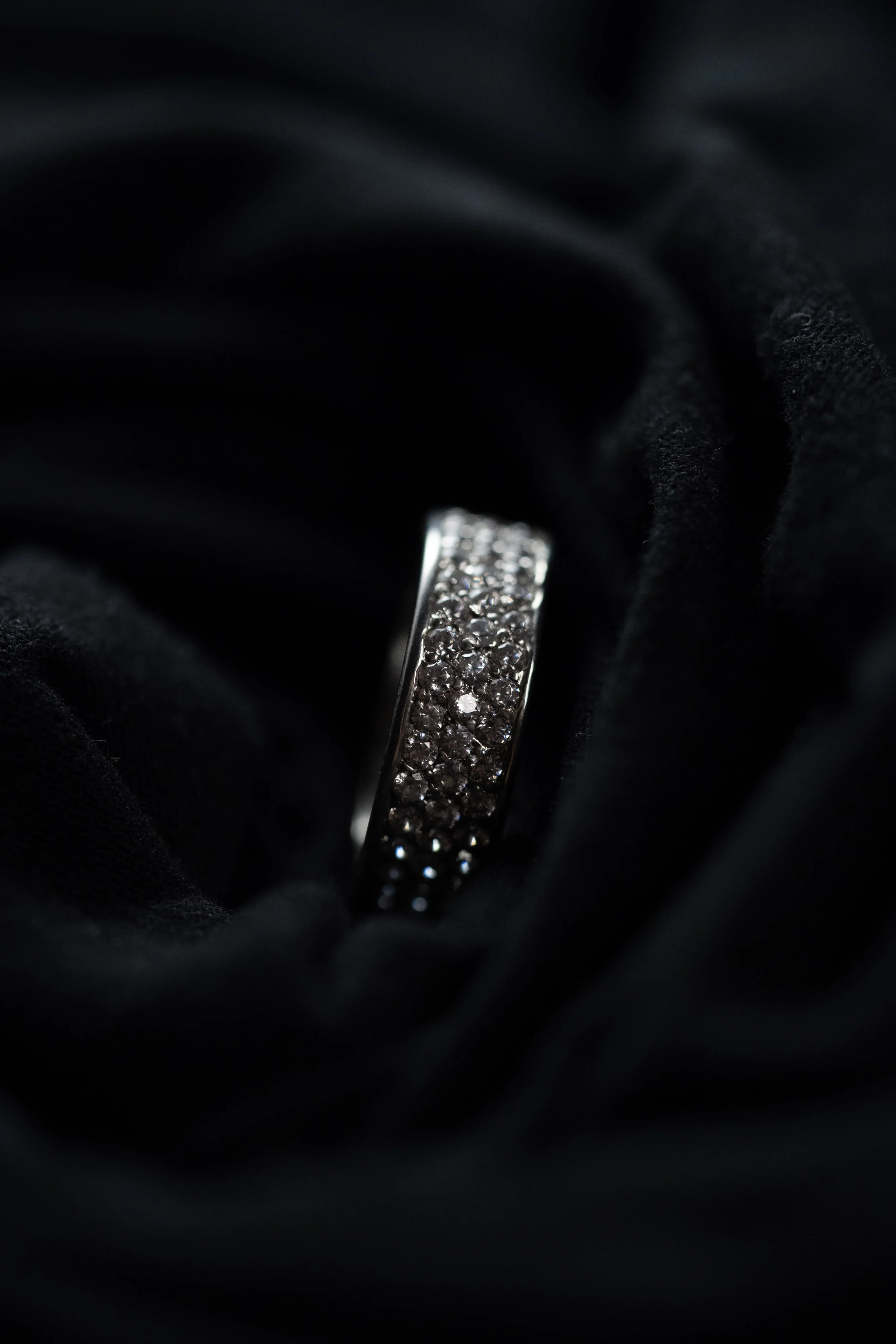 Close-up of a silver ring with multiple small diamonds, resting on black fabric.