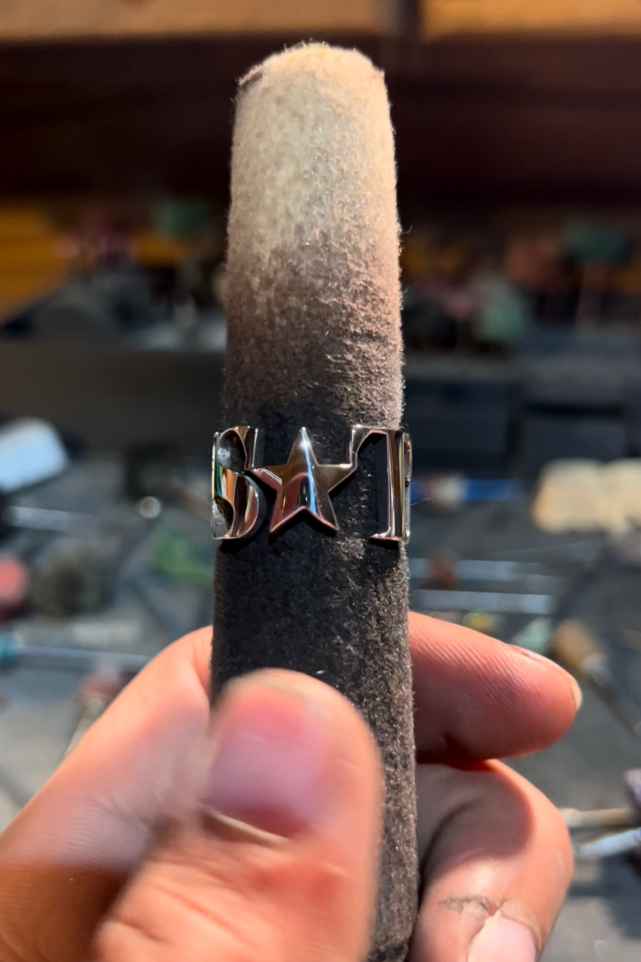 Close-up of a finger holding a black foam-covered cylindrical object with a metal ring around it, engraved with the word 'BOY' and a star.