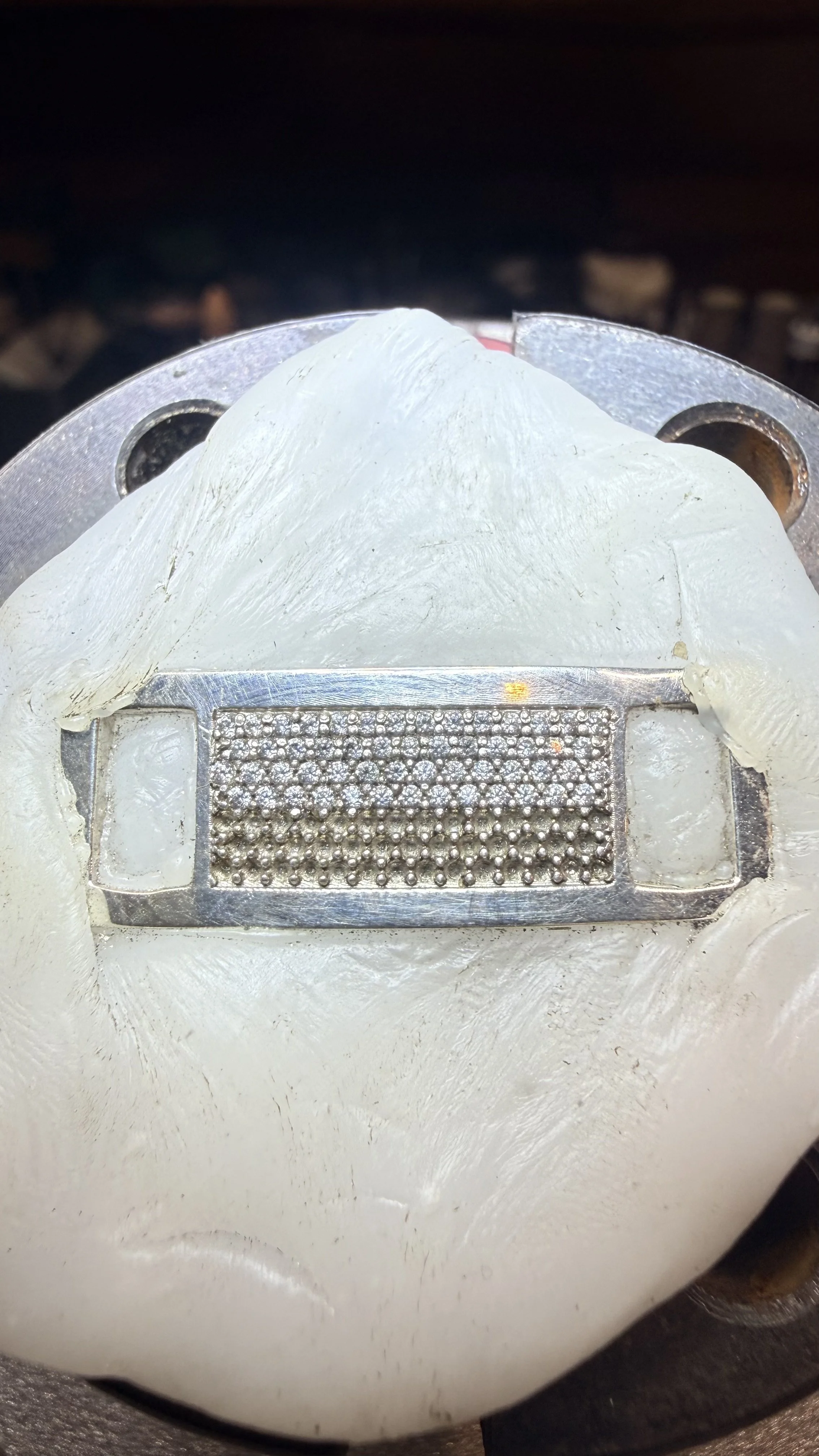 Close-up of a metal grinding tool with a rectangular grid of tiny metal balls, partially covered by a white substance, possibly wax or lubricant.