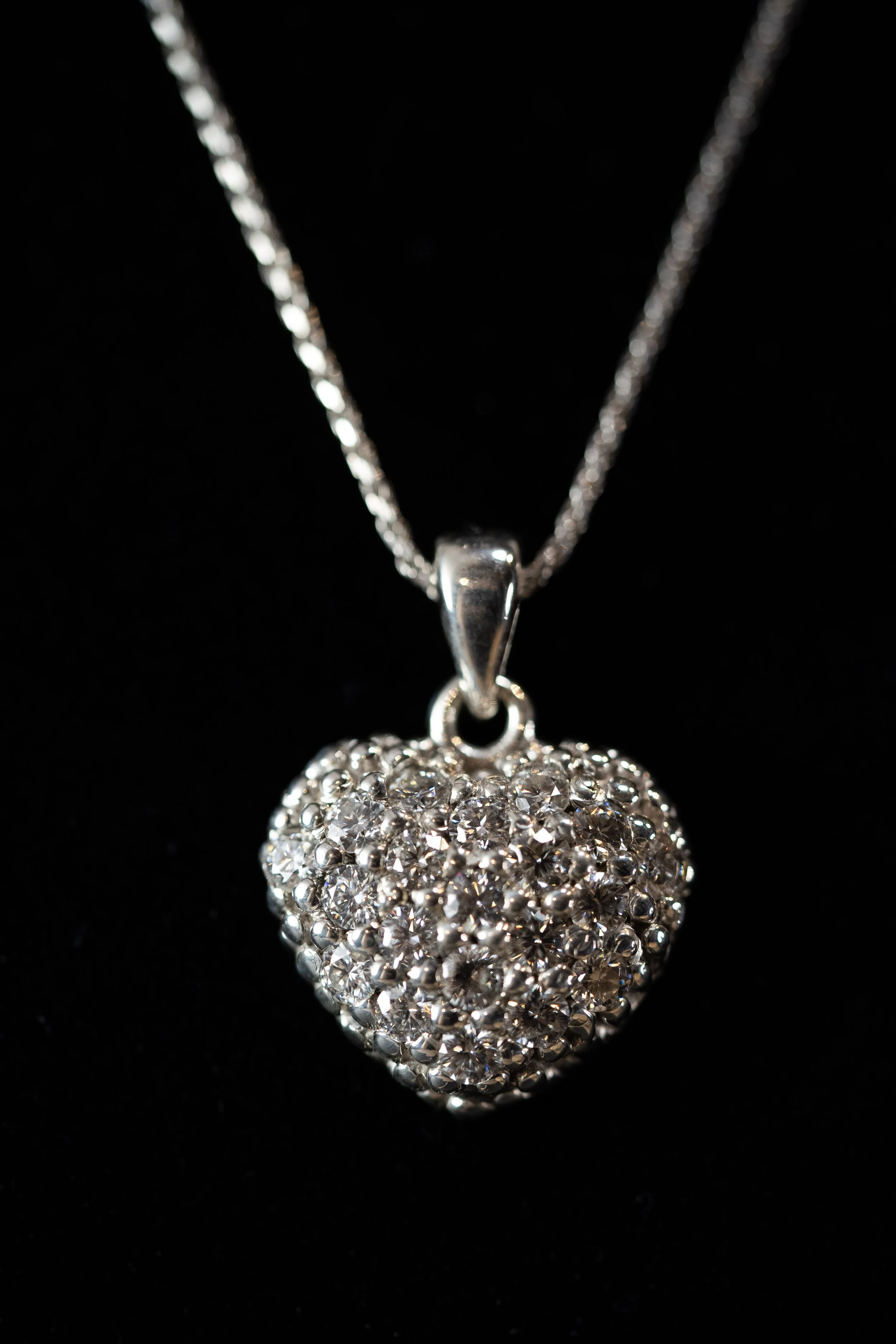 Silver heart-shaped pendant necklace decorated with small sparkling rhinestones on a black background.