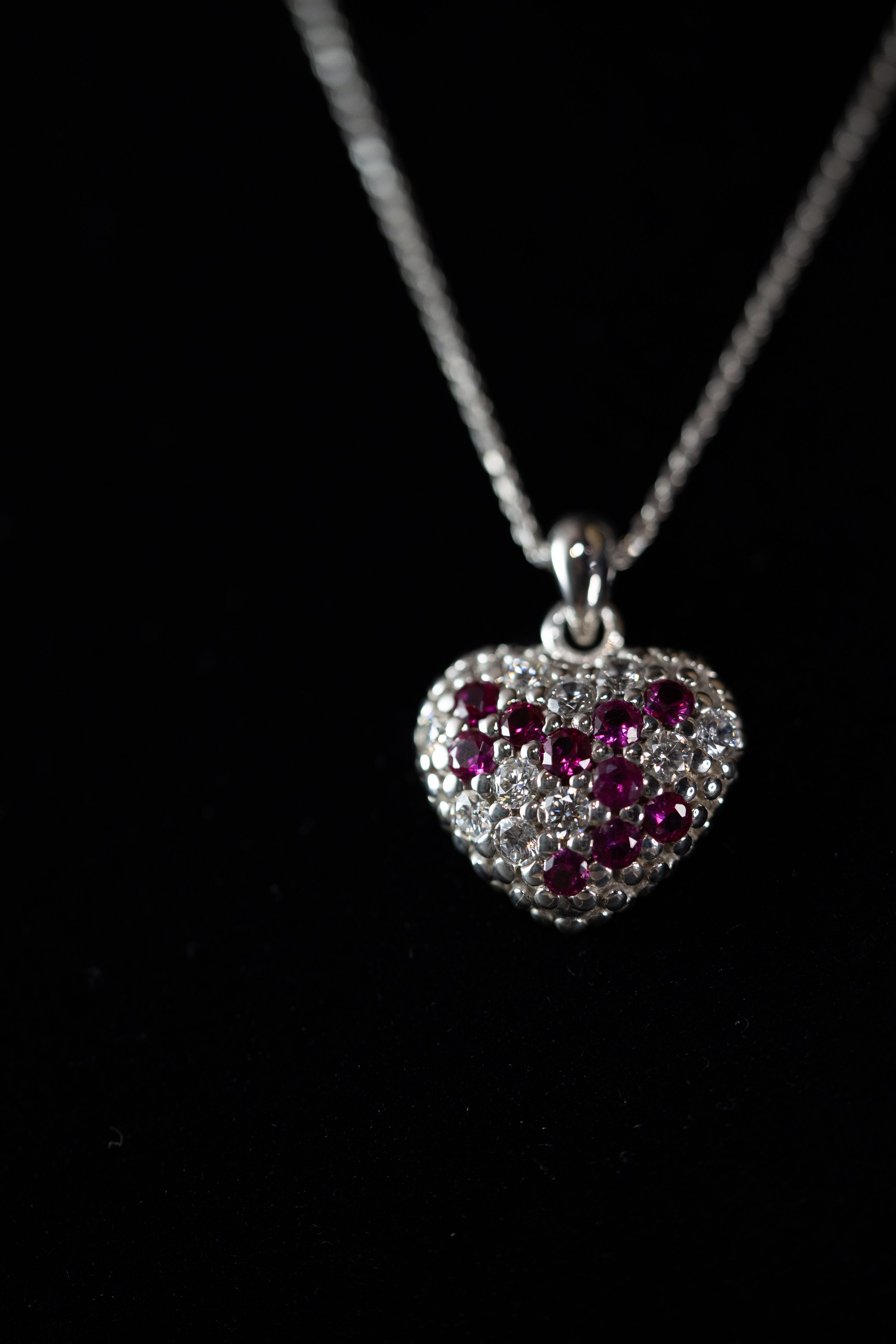 Silver heart-shaped pendant necklace with pink and clear gemstones on a black background.