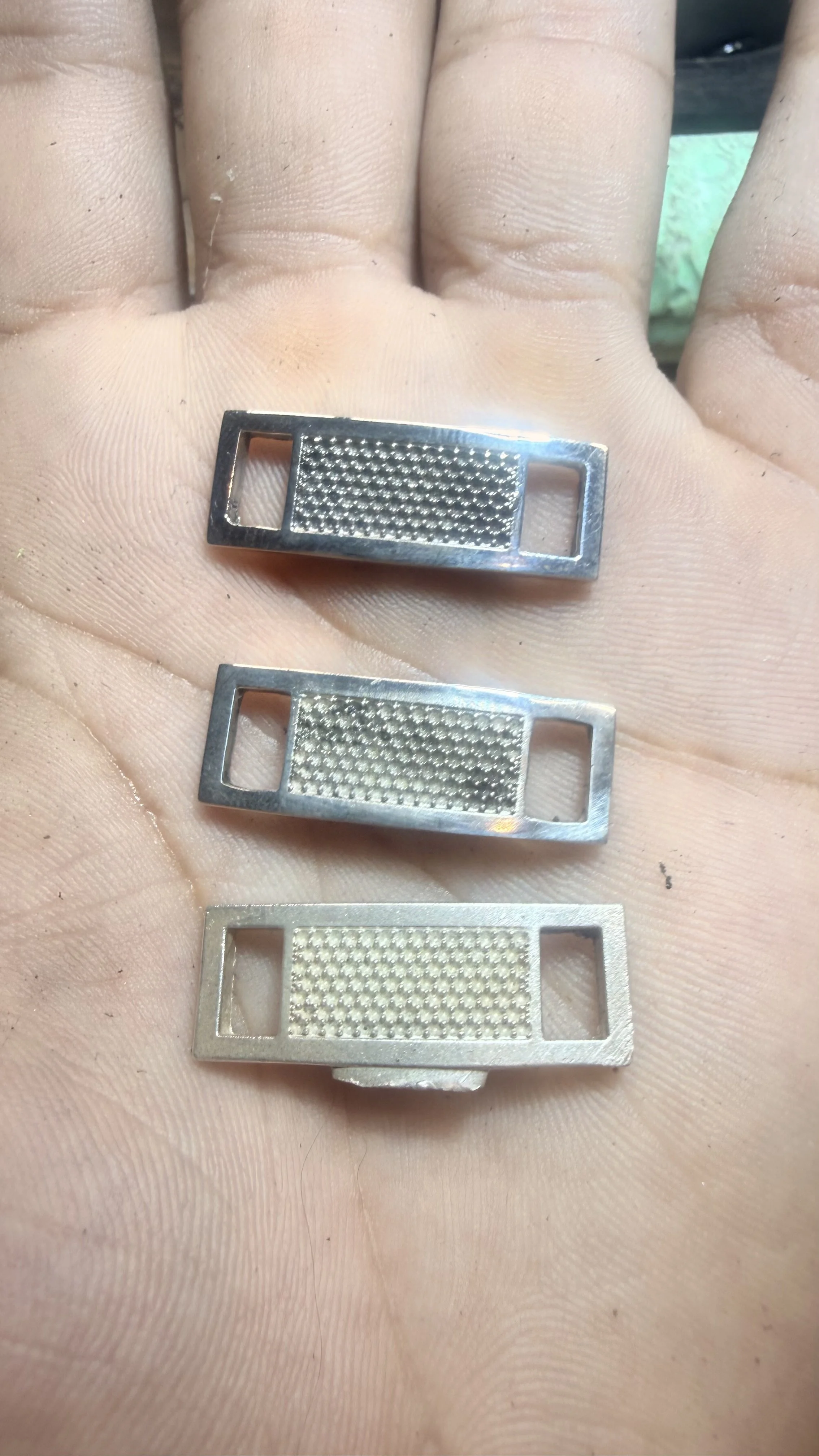 Close-up of three metal razor blade holders in a person's hand, showing textured blades with rectangular openings on each side.